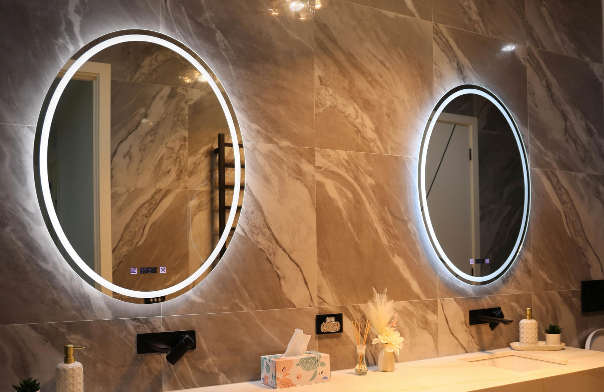 Backlit round bathroom mirrors with LED lighting, mounted on marble-look wall tiles above a modern double vanity.