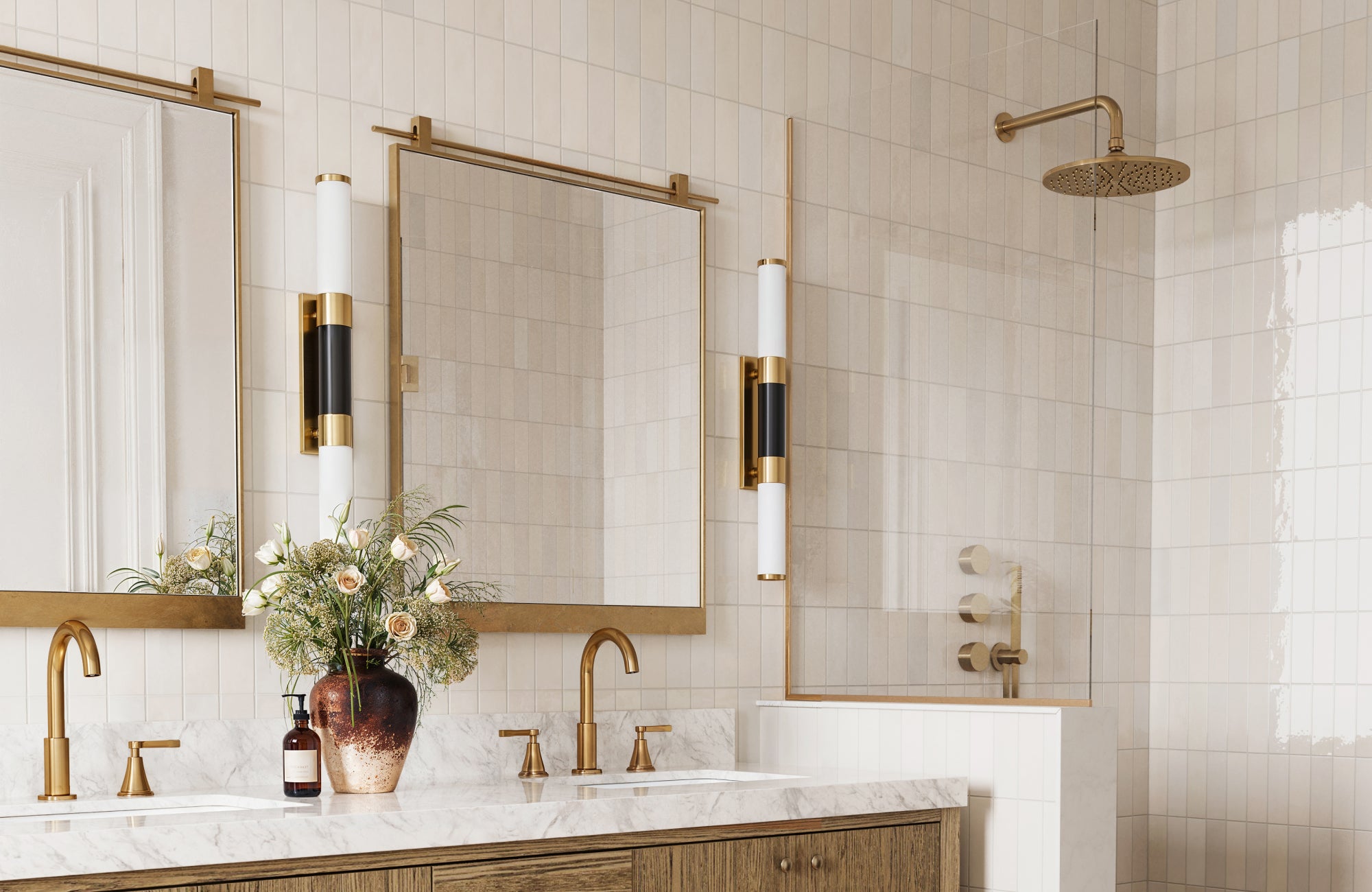 Rectangular bathroom mirrors with thin gold frames, mounted on brass rails above a double vanity with a marble top.