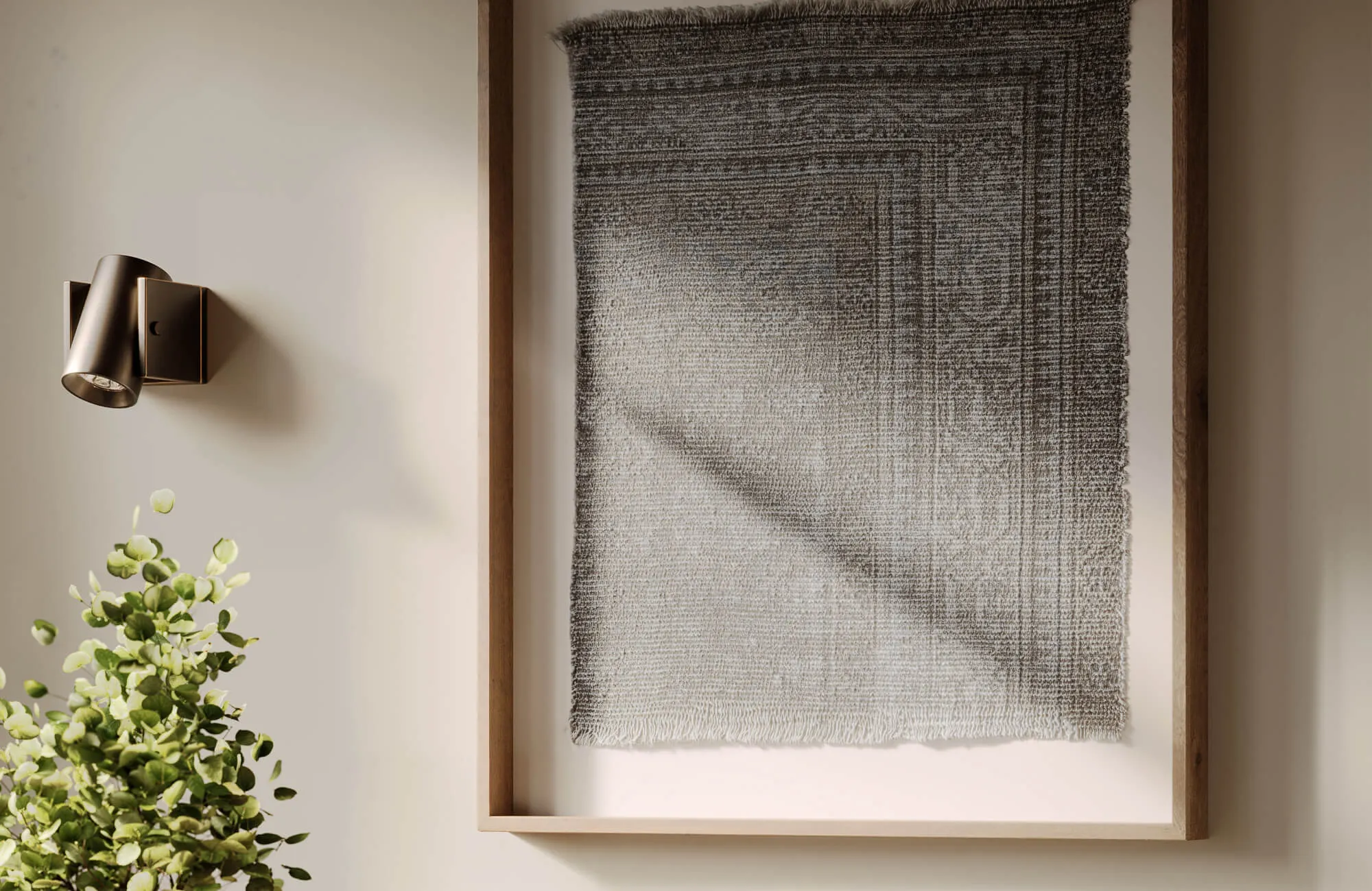 Framed woven wall art with a faded gray pattern mounted on a light bathroom wall, paired with a bronze sconce and leafy green accents.