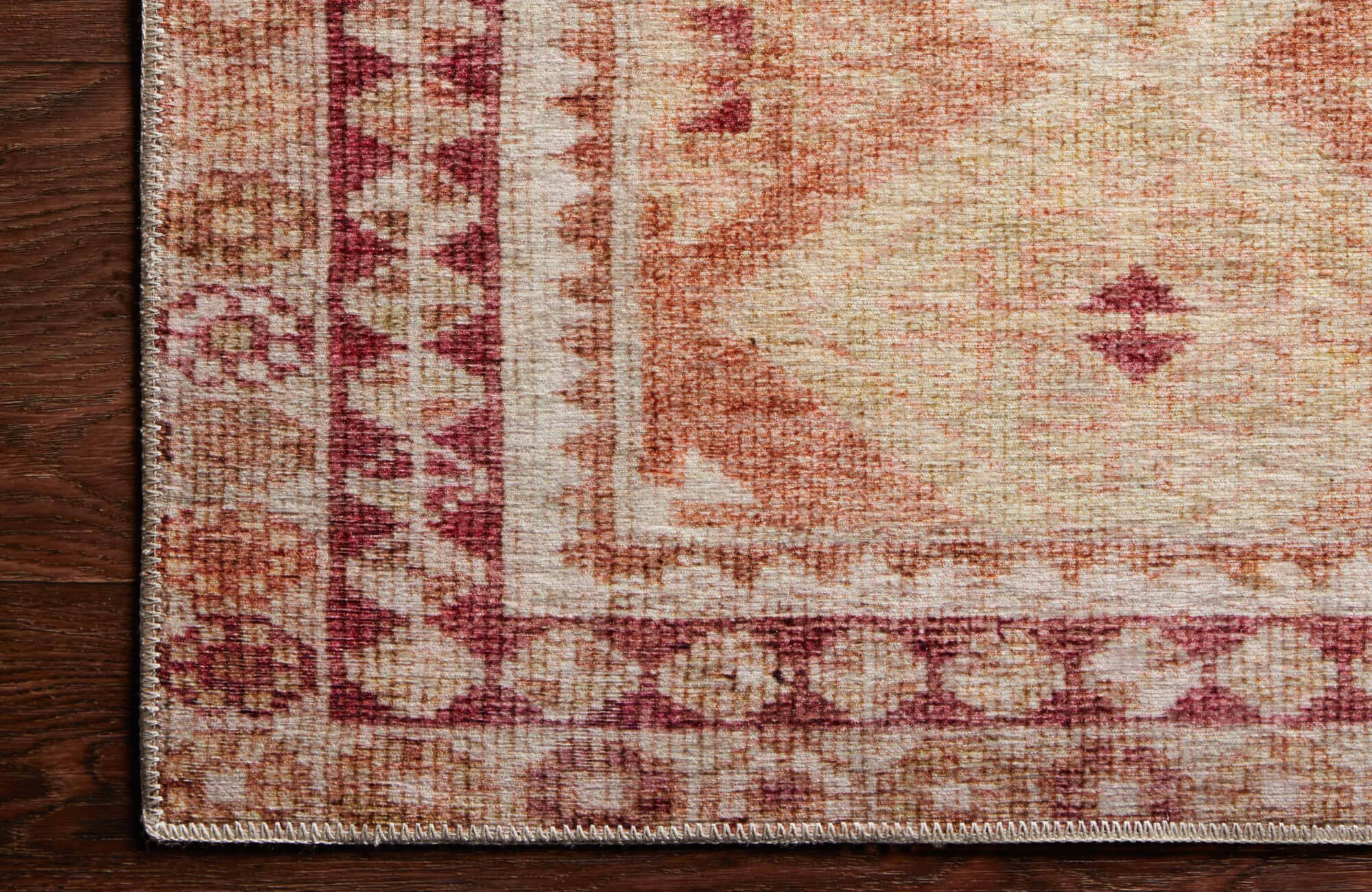 Corner detail of a warm-toned vintage area rug with red, rust, and beige patterns on a dark hardwood floor for a cozy room atmosphere