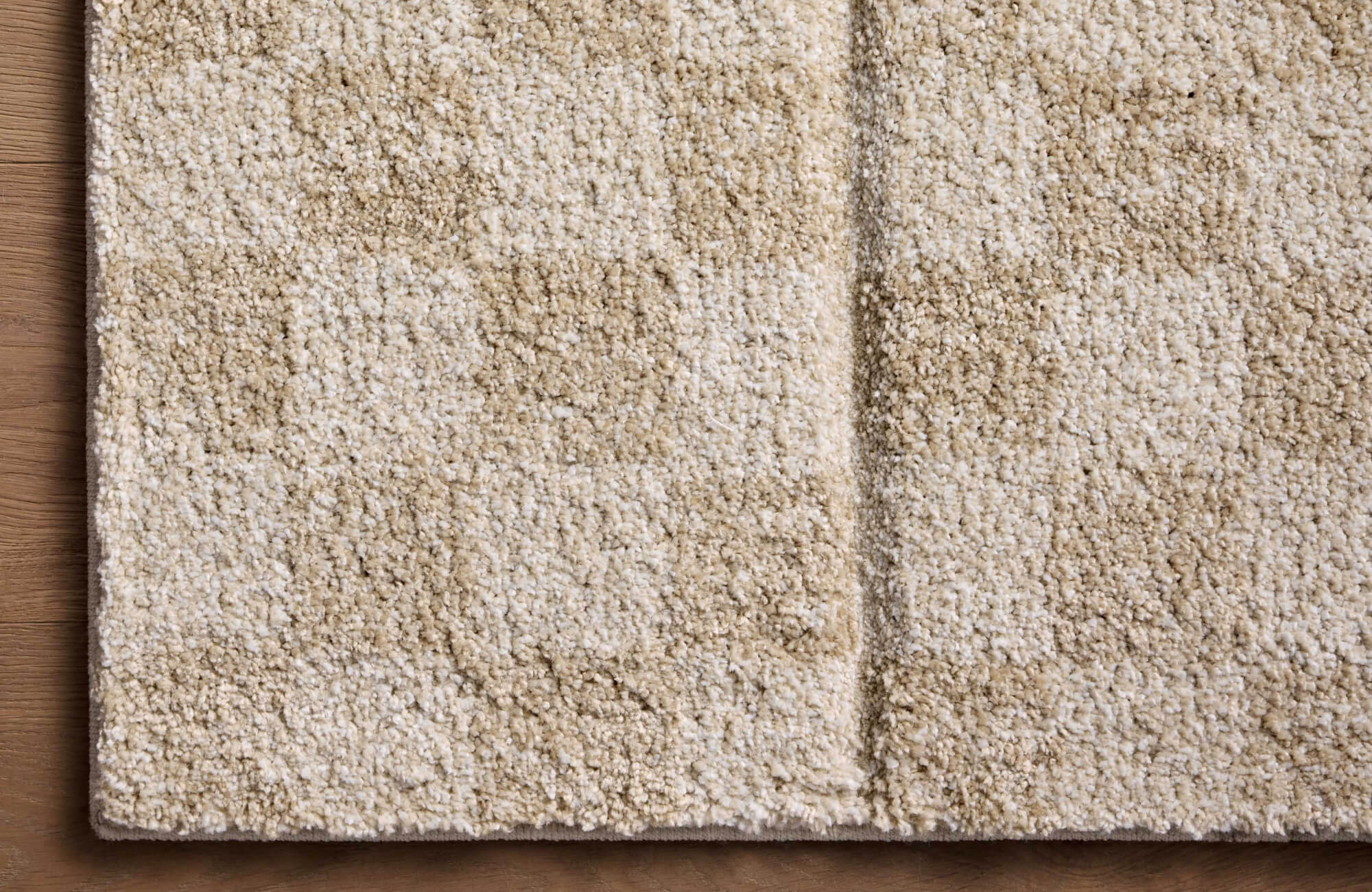Close-up of soft beige and cream checkered shag rug on light oak wood floor, ideal for adding cozy texture and warmth to any neutral space