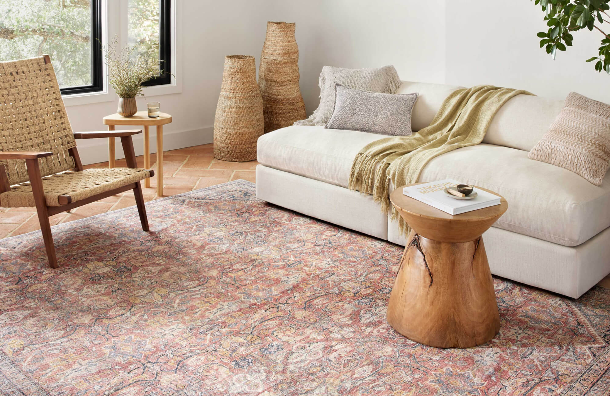 Cozy living room with soft cream sectional, terracotta tile floors, warm pink vintage rug, natural wood accents, and woven lounge chair