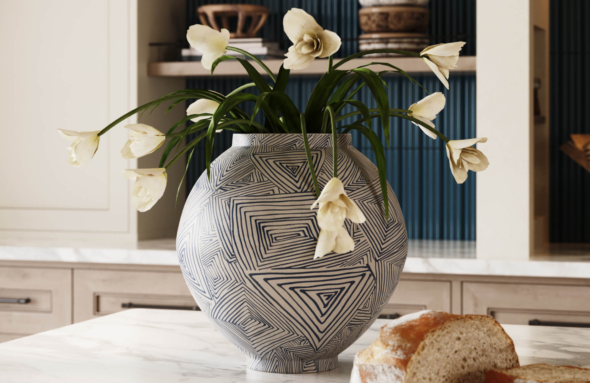 Large white vase with blue geometric linework holding cream flowers in front of a dark blue reeded tile backdrop and neutral kitchen cabinetry.