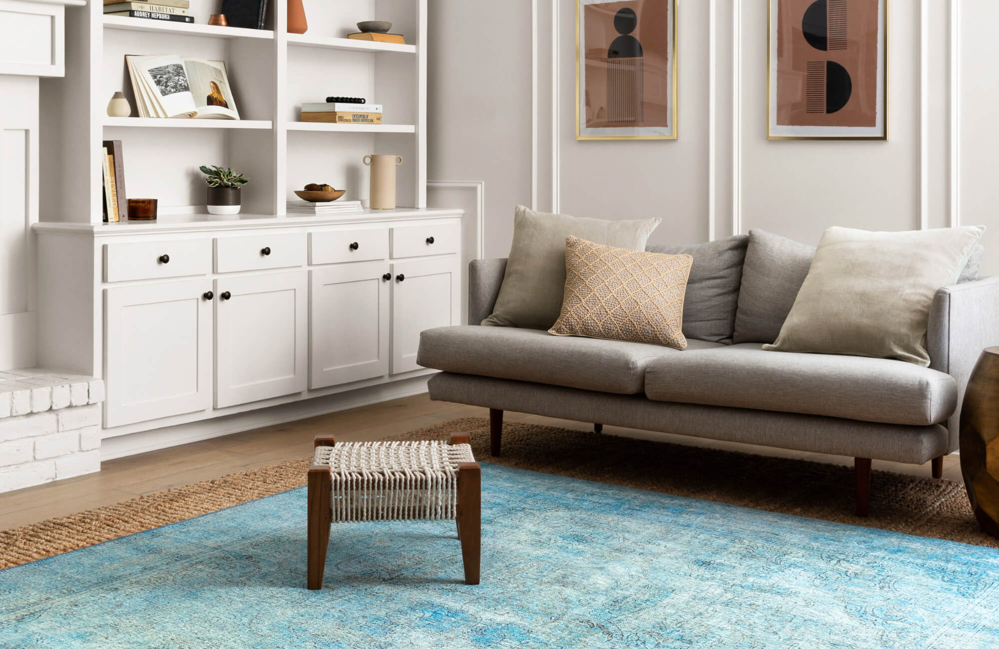 Modern living room with a light blue rug, gray sofa, neutral pillows, and built-in white shelving creating a calm, contemporary look.