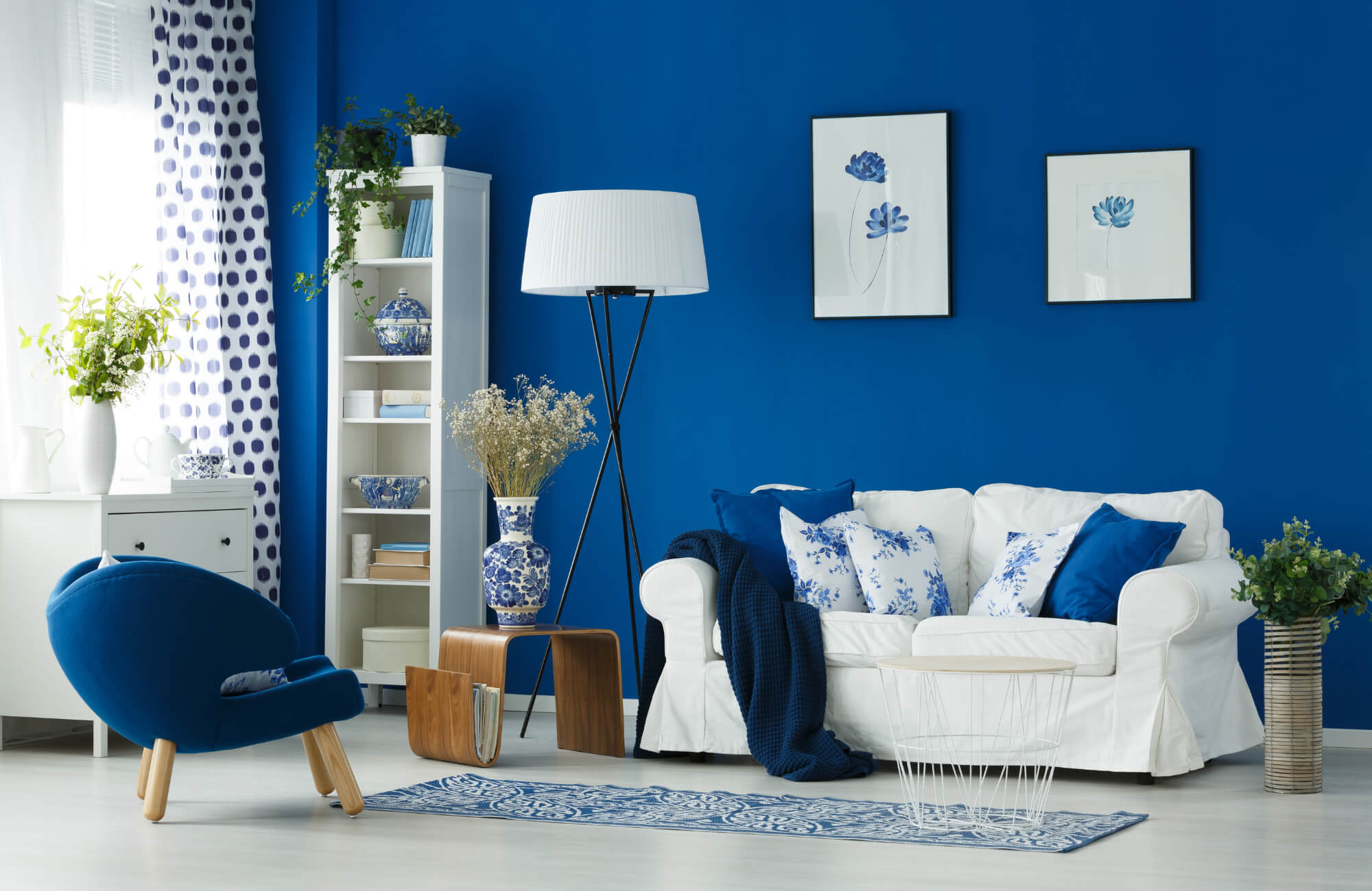 Bright living room with bold blue walls, white sofa with patterned pillows, a blue rug, and modern accents creating a vibrant, cohesive space.