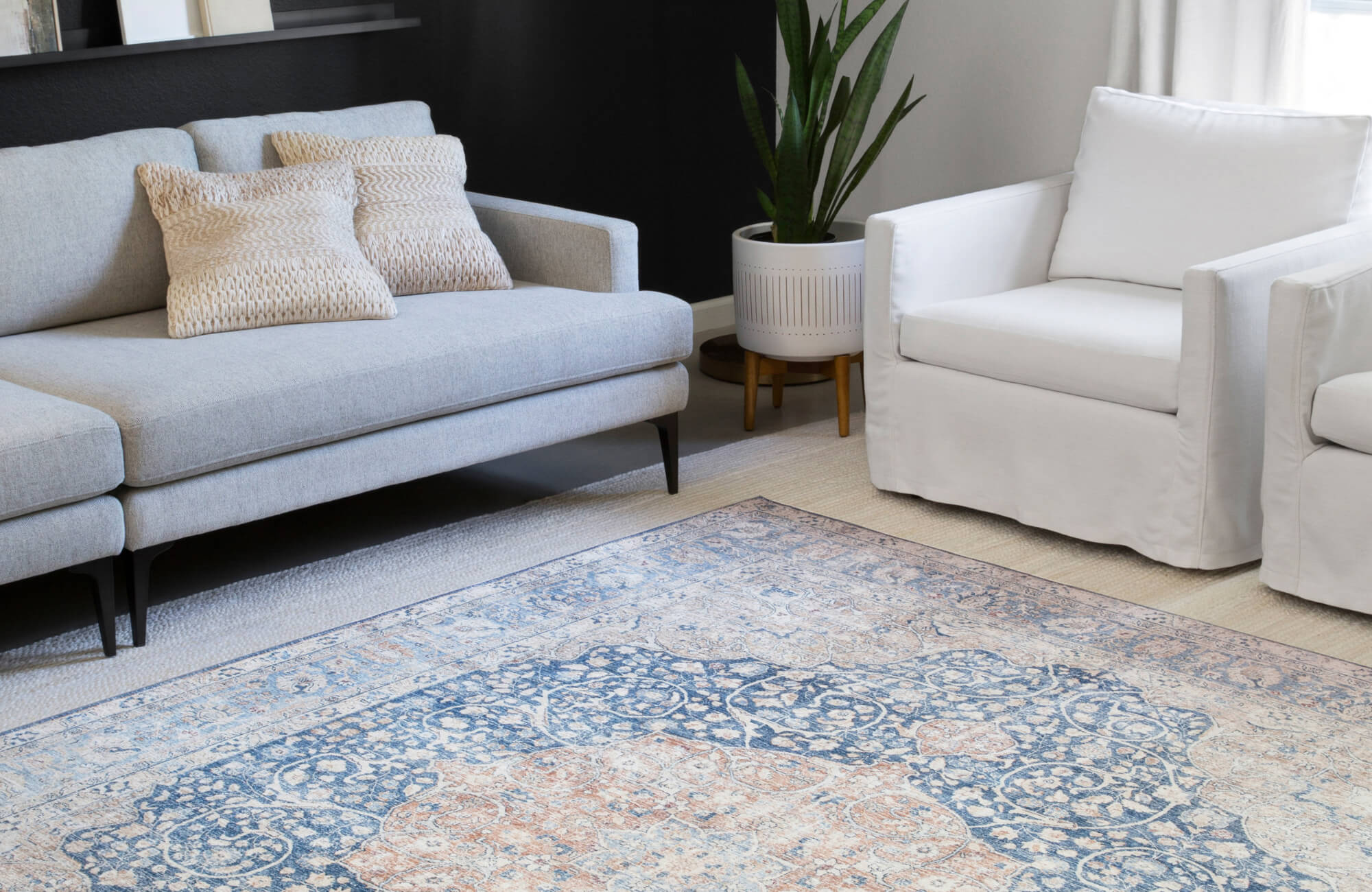 Contemporary living room with a patterned blue and beige rug, light gray sofa, white armchair, and neutral accents for a modern look.