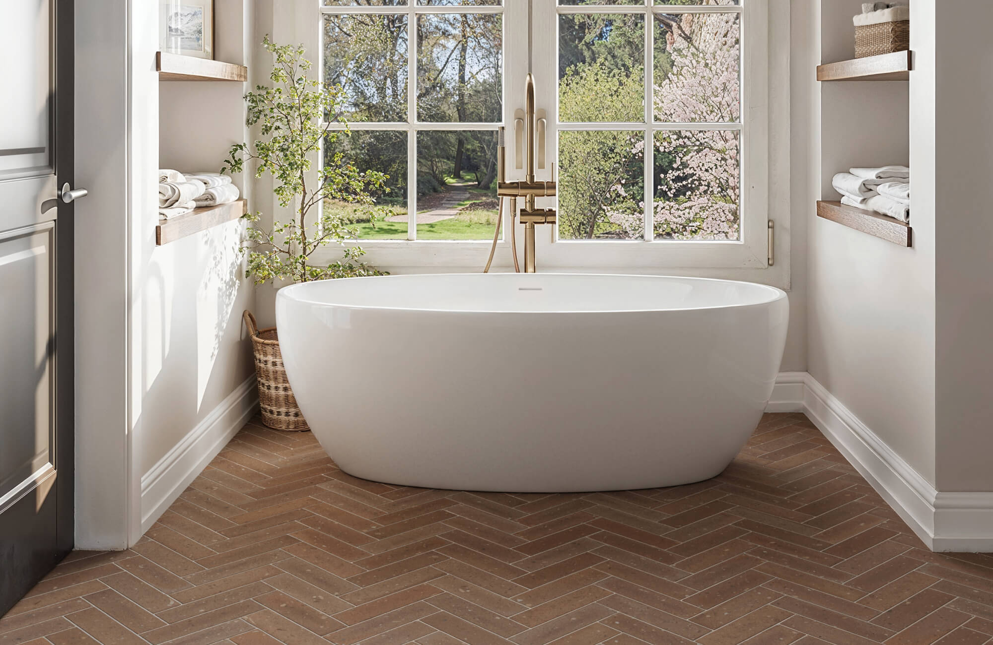 Bathroom with white freestanding tub, large grid windows, and warm brown herringbone tile floor that enhances natural light and neutral tones