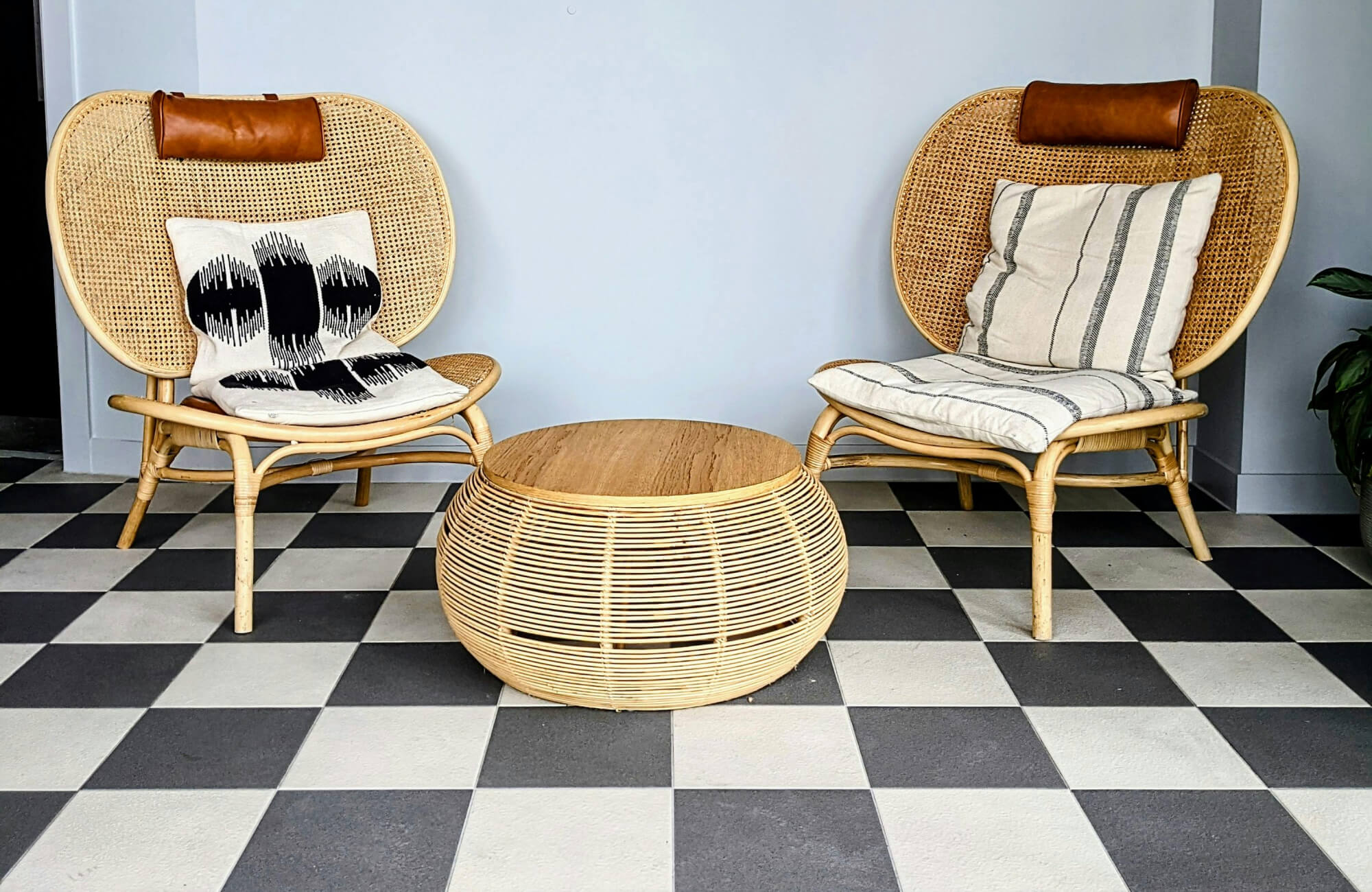 null Indoor seating nook with woven rattan chairs, a round slatted table, and a bold black and white checkered tile floor.