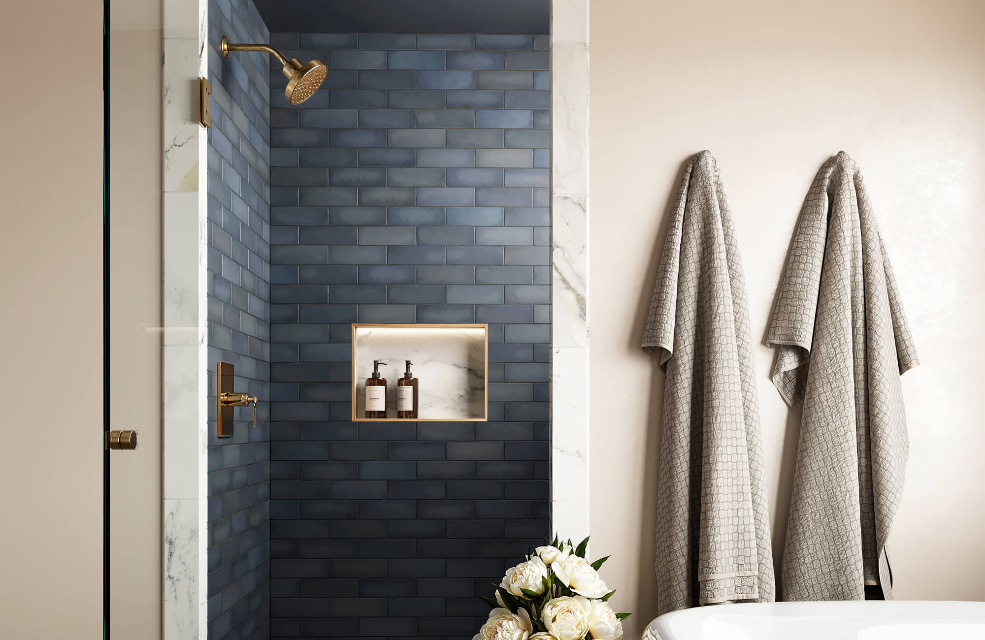 null Shower with matte blue subway tile, marble shower niche and trim, brass fixtures, and soft beige wall with textured taupe towels