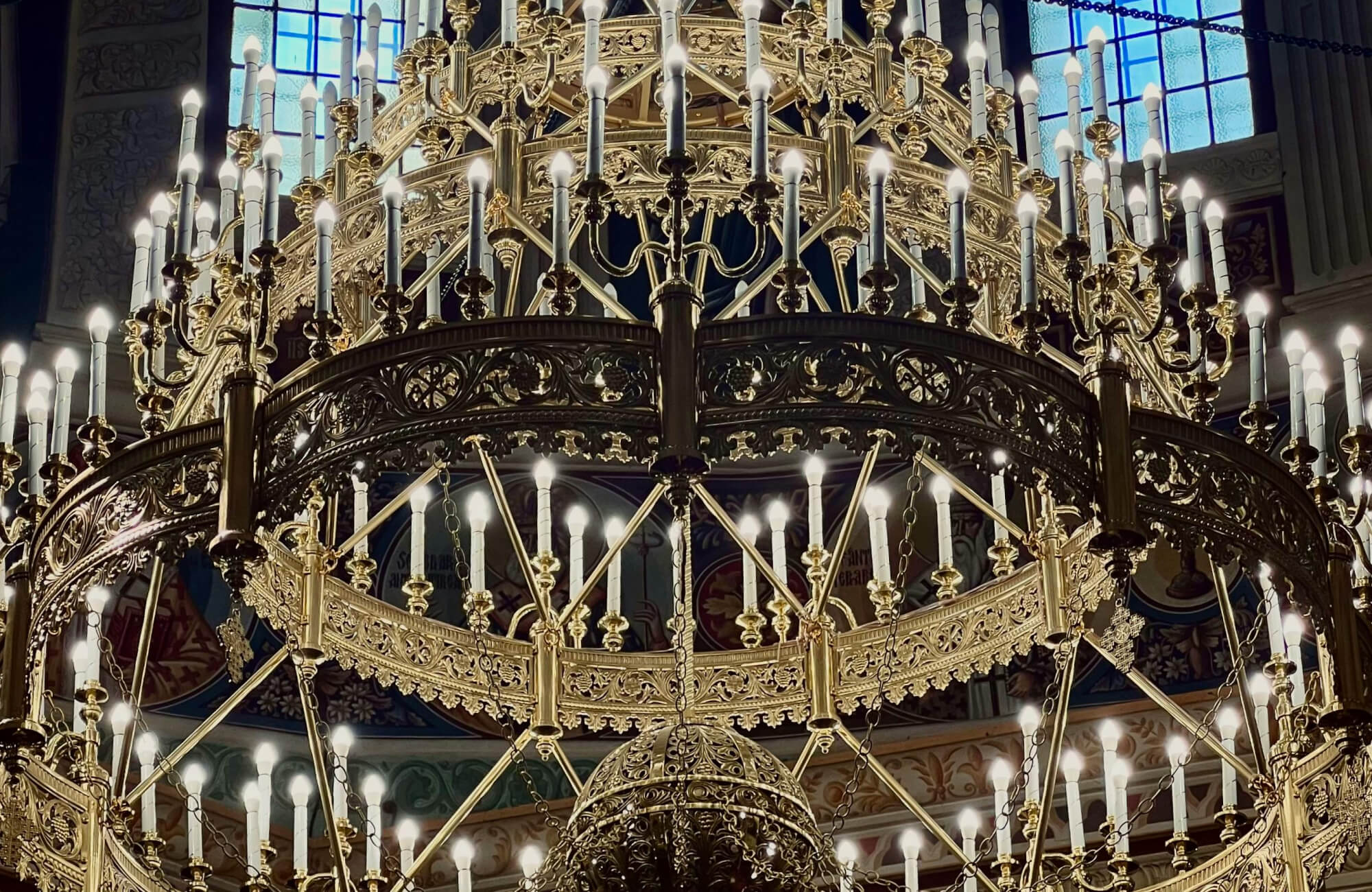 null Magnificent gold chandelier with intricate filigree details and tiers of glowing candle-style lights, exuding regal grandeur in a historic setting.