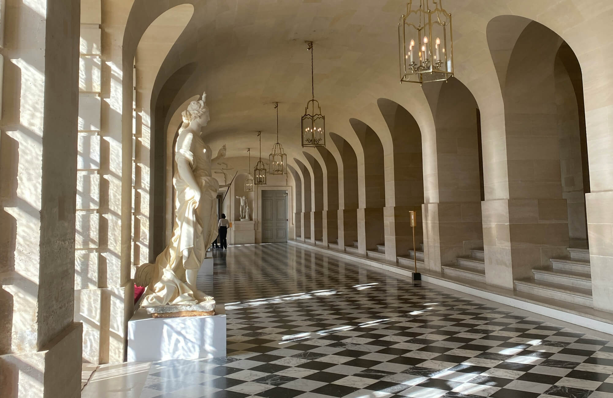 null Elegant hallway with a black and white checkerboard floor, arches, and classical statues in a sunlit, historic building.
