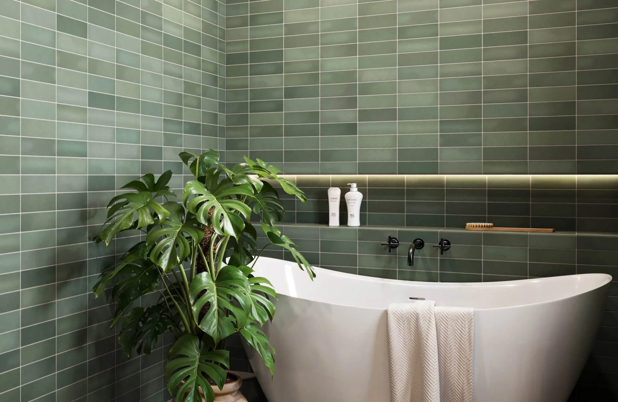 Modern bathroom with rich moss green subway tile walls in a stacked grid pattern, a sleek white freestanding tub, and lush monstera plant decor.