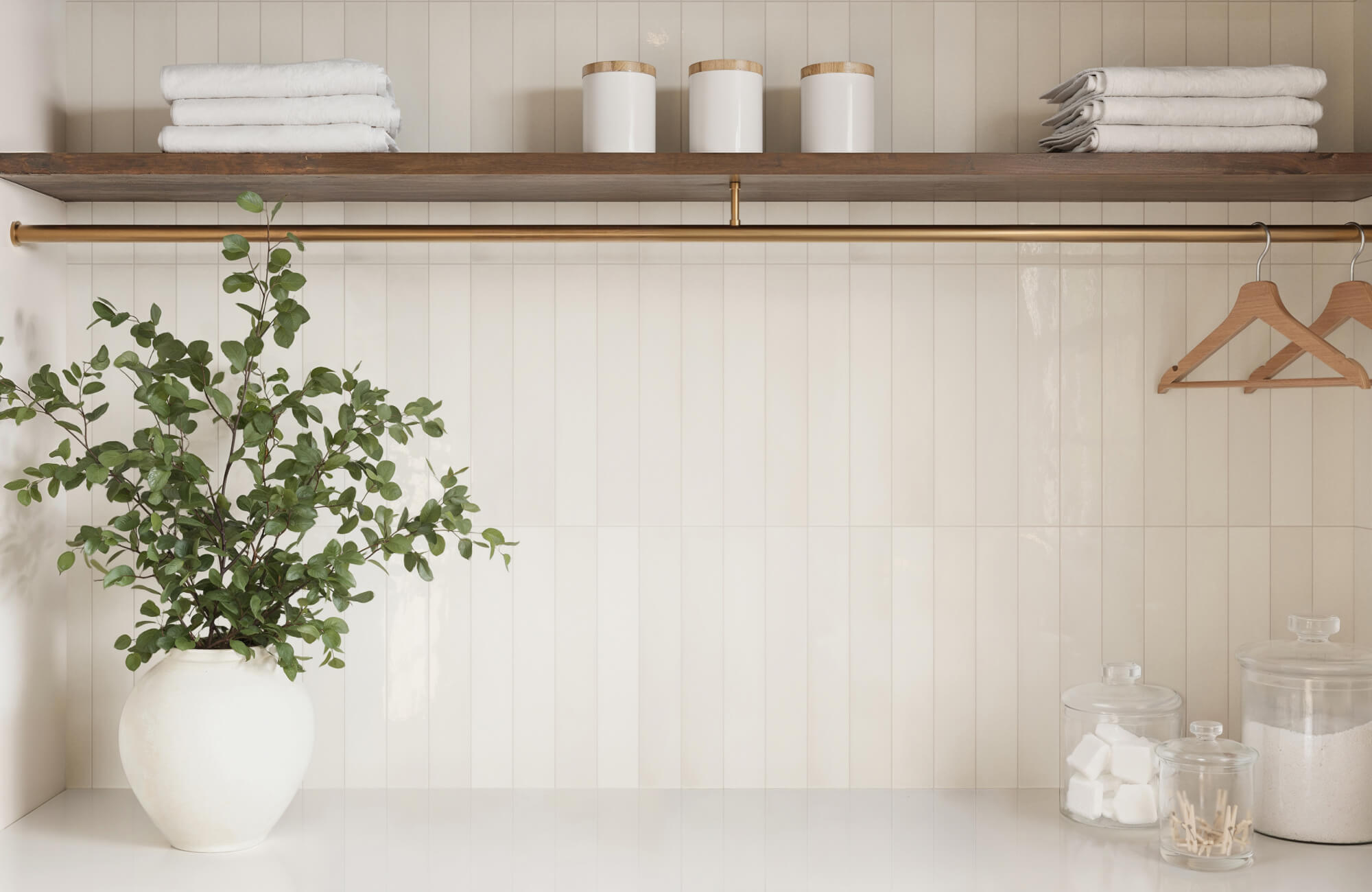 Vertical white subway tiles with ivory grout offer a calm, minimal look in this laundry nook with brass and wood finishes.