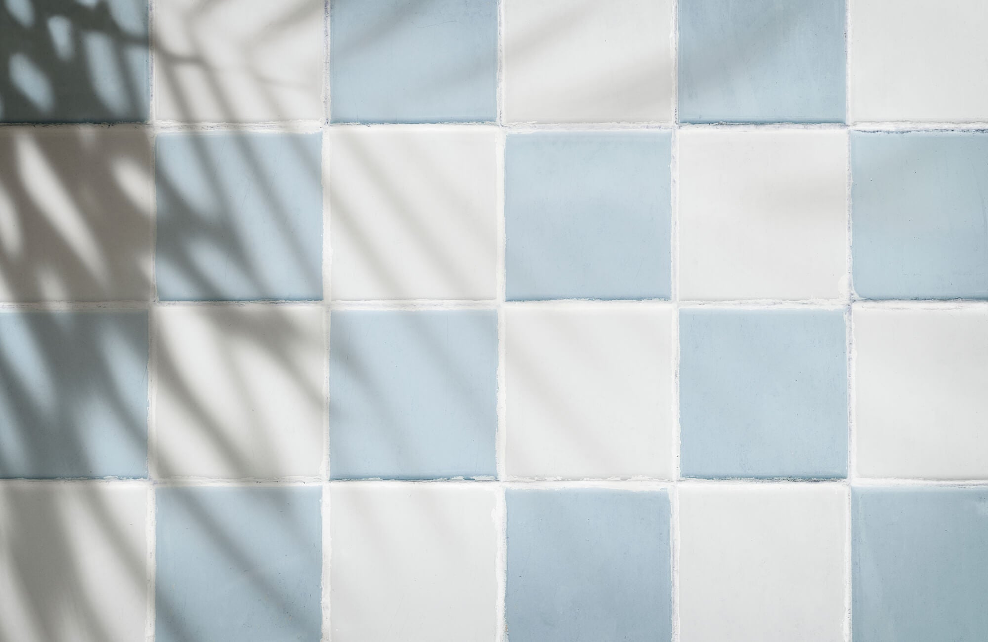 Soft blue and white square tiles arranged in a checkerboard layout, finished with slightly uneven white grout lines that create a handmade, textured look between each tile.