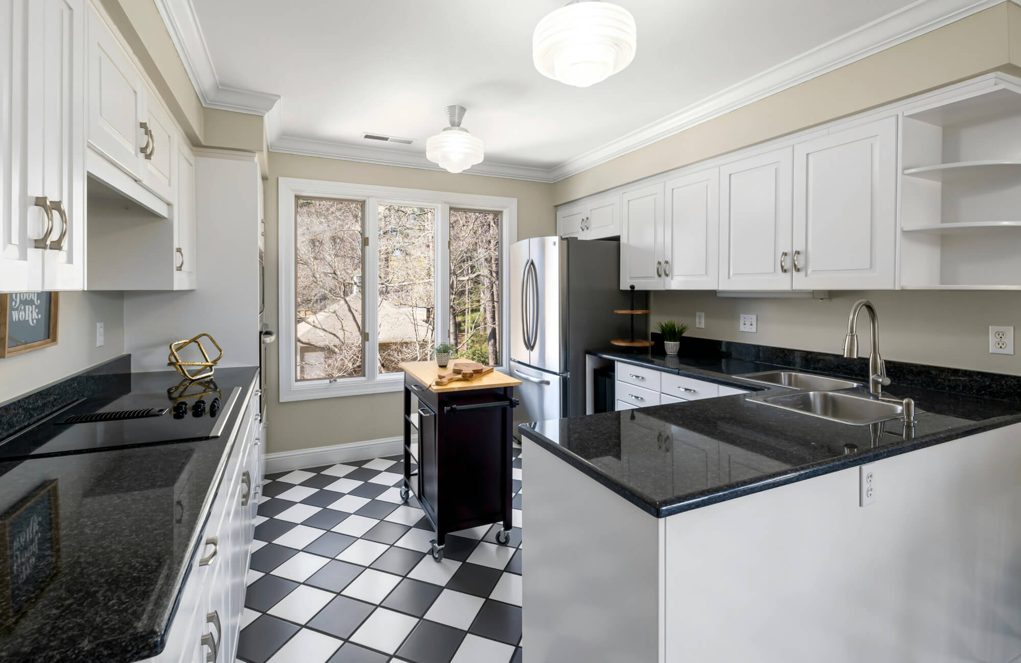 Bright, airy kitchen with white cabinetry and sleek black countertops, featuring black and white floor tiles in a classic checkerboard pattern, installed with black grout lines that create a bold, high-contrast foundation throughout the space.