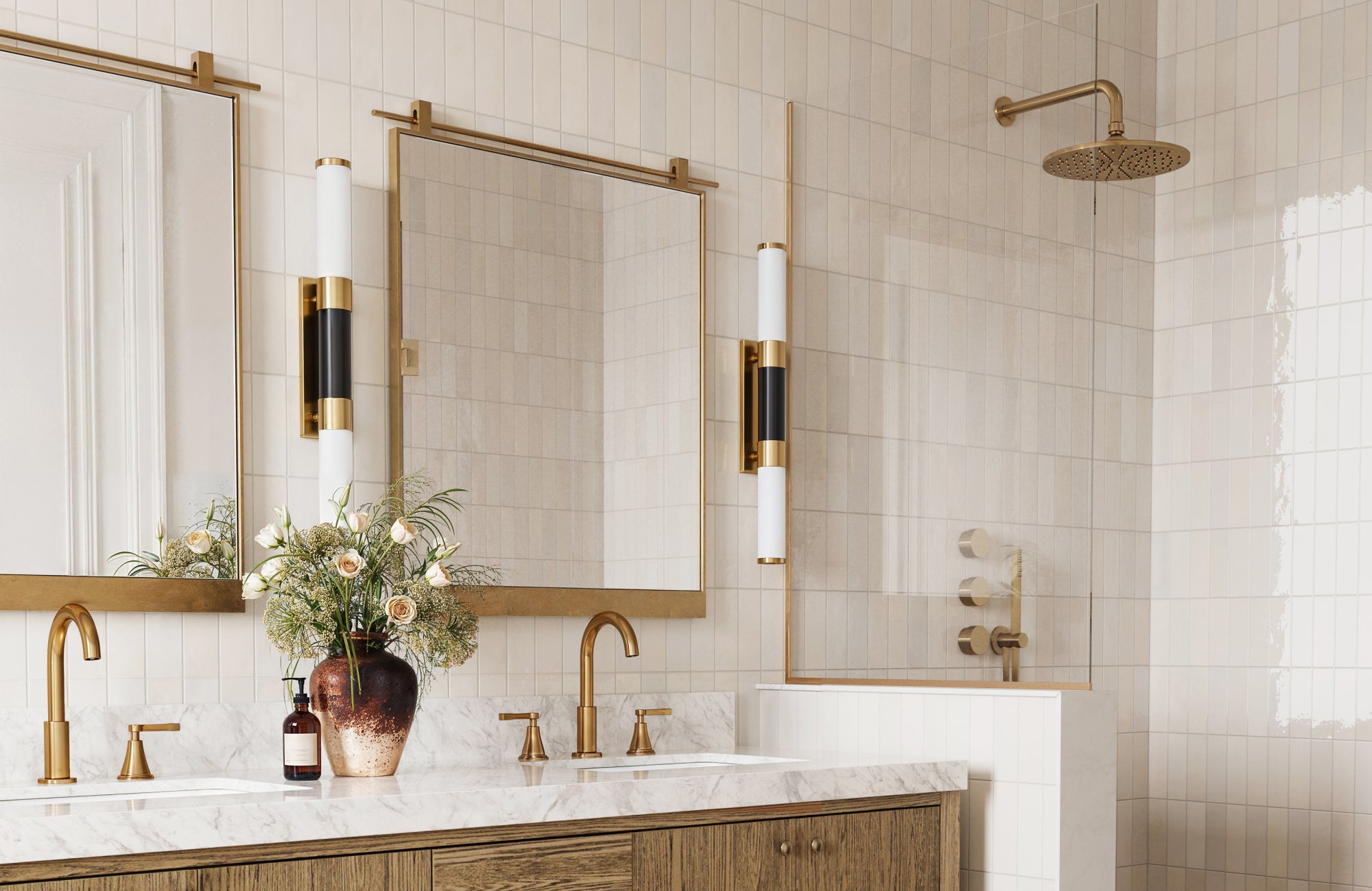 null Sleek vertical sconces with black and white detailing frame a double mirror vanity in a warm, neutral tile bathroom.