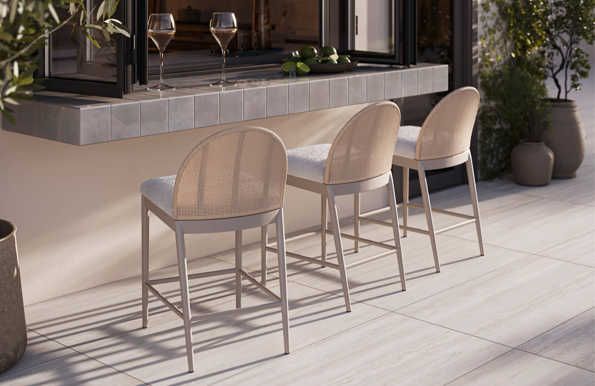 null Outdoor counter with three woven bar stools, a tiled serving ledge, light paver flooring, and open glass doors.