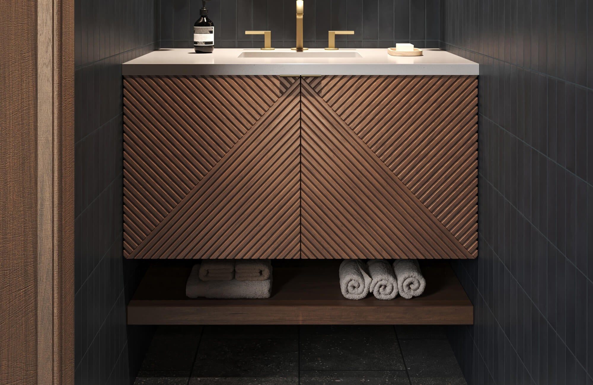 Modern vanity with chevron wood front set against deep charcoal ceramic tile walls and sleek brass fixtures.