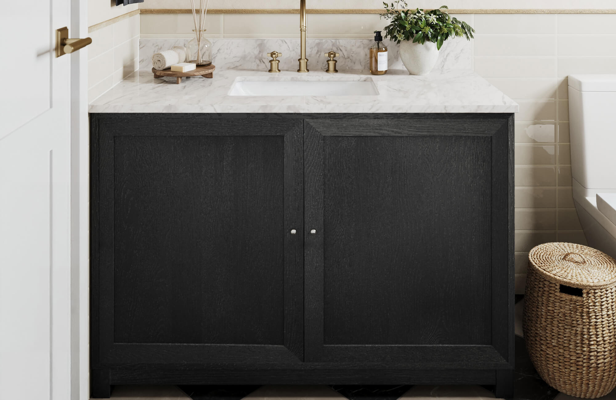 Black wood vanity with marble countertop set against cream ceramic wall tiles and brushed brass faucet.