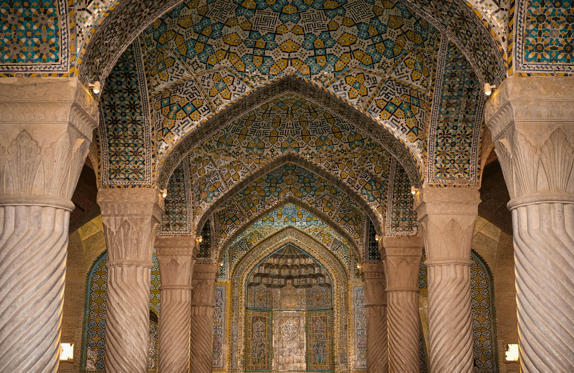 Intricately tiled Persian-style interior with colorful geometric mosaic patterns across vaulted ceilings and grand archways.