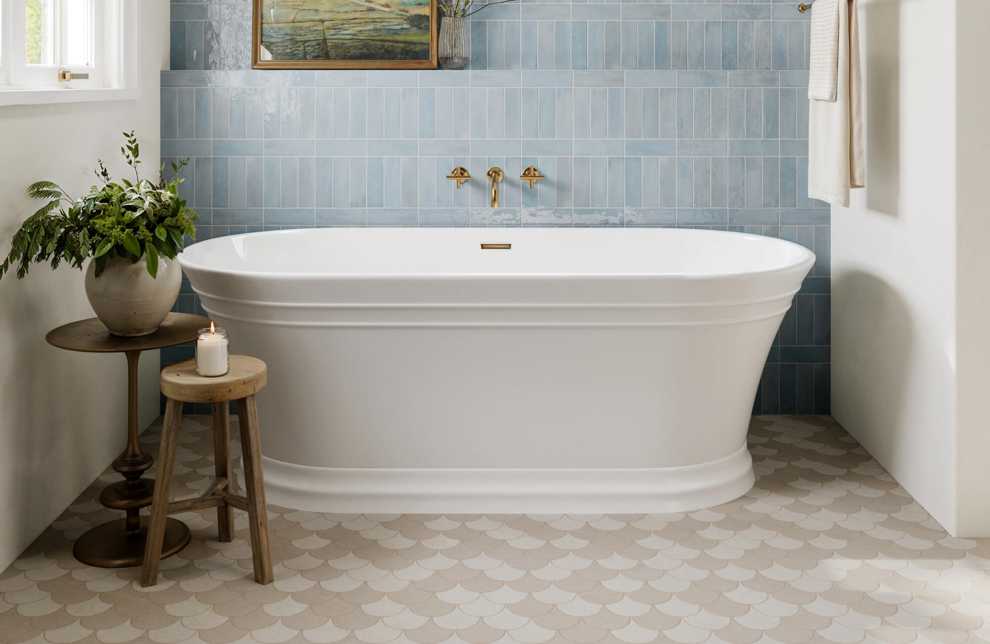 Serene bathroom with a white freestanding tub, scalloped beige mosaic floor tiles, and vertical blue wall tiles with gold fixtures.
