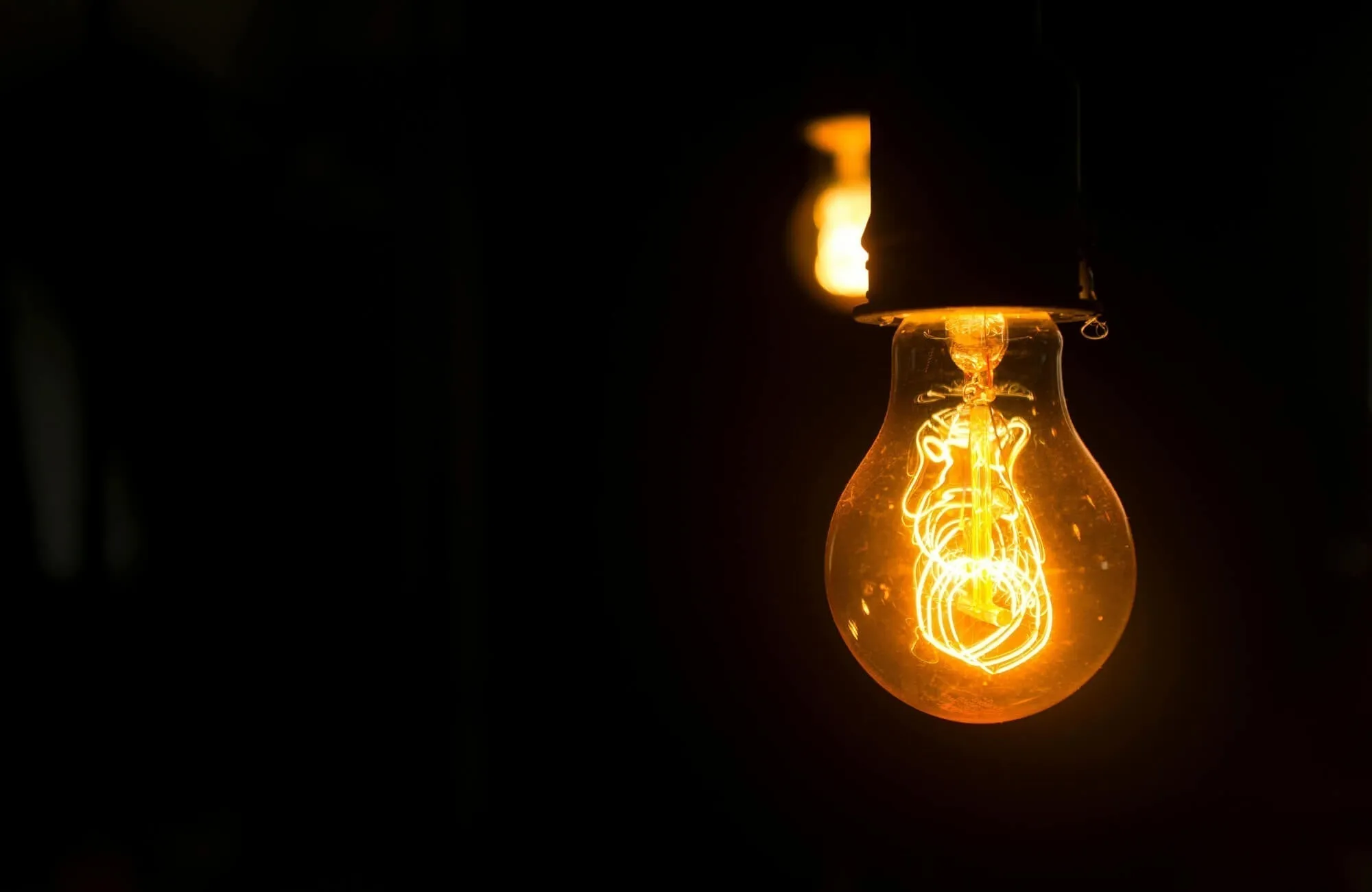 A warm amber light bulb illuminated in the dark, highlighting its glowing filament detail.