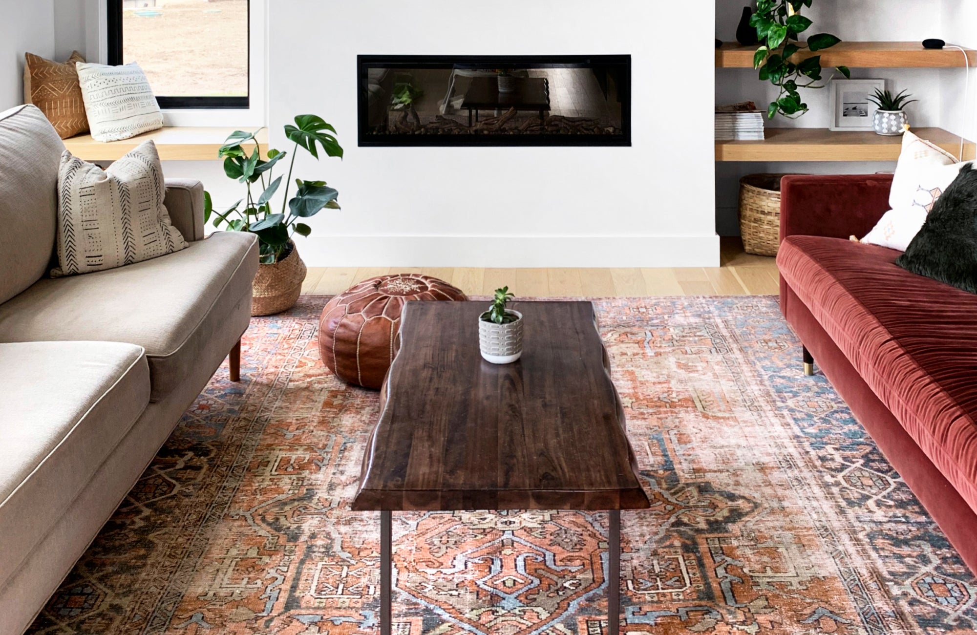 Warm, earthy living space with a richly patterned rug centered between two sofas and a narrow black fireplace.