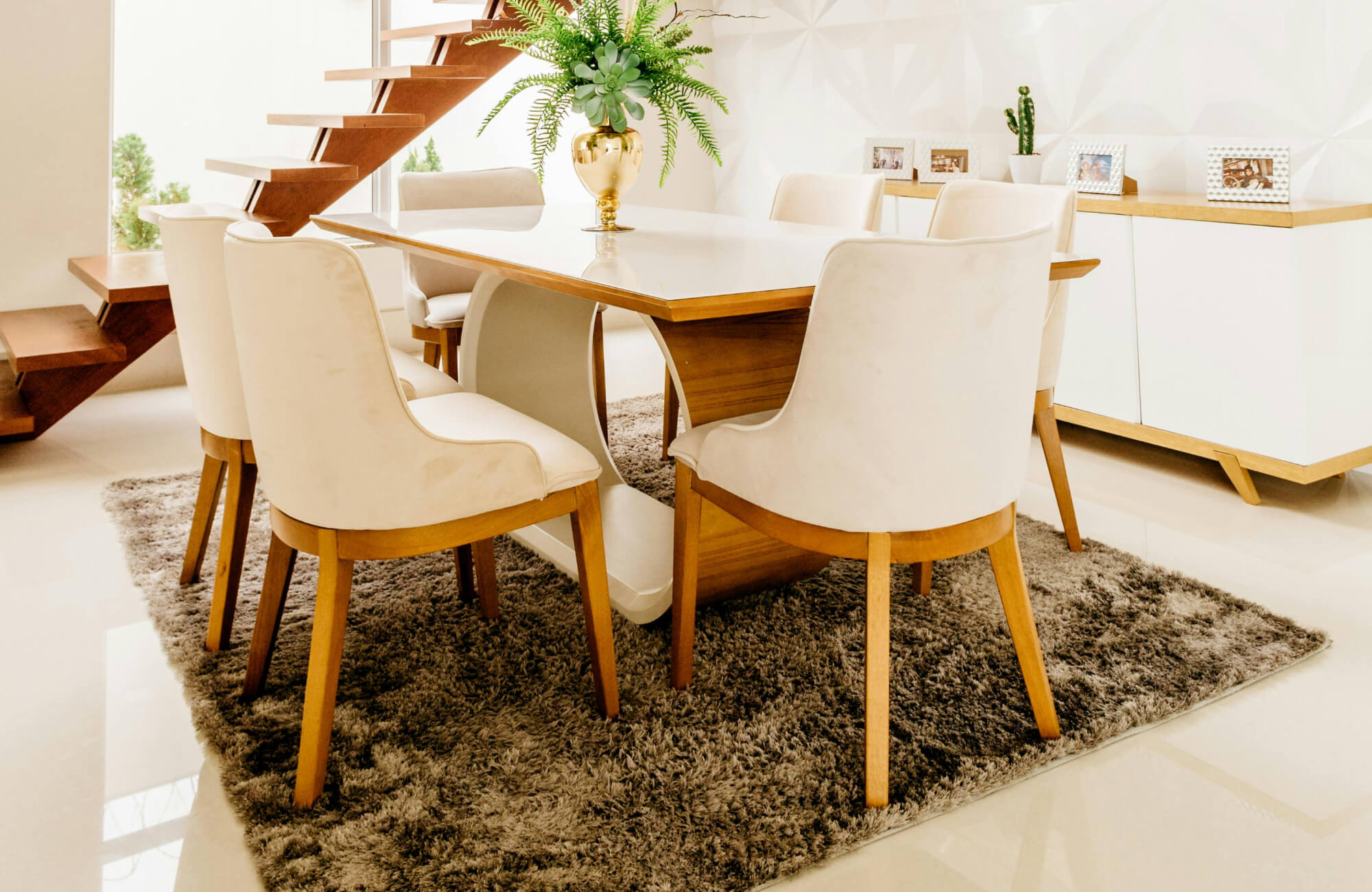 Bright dining area with a soft shag rug grounding a wood and white dining set, styled over glossy white tile flooring.