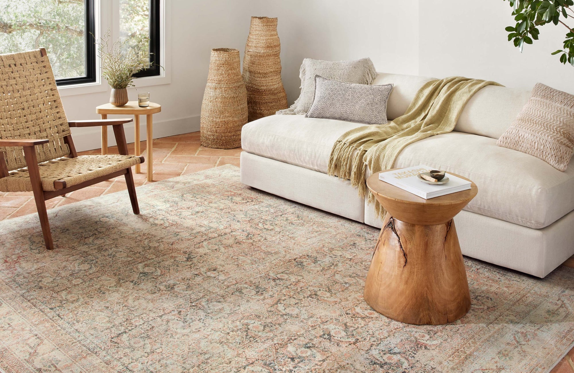 Light-filled room with a pale vintage rug set over terracotta tiles, softening a neutral sofa and natural textures.