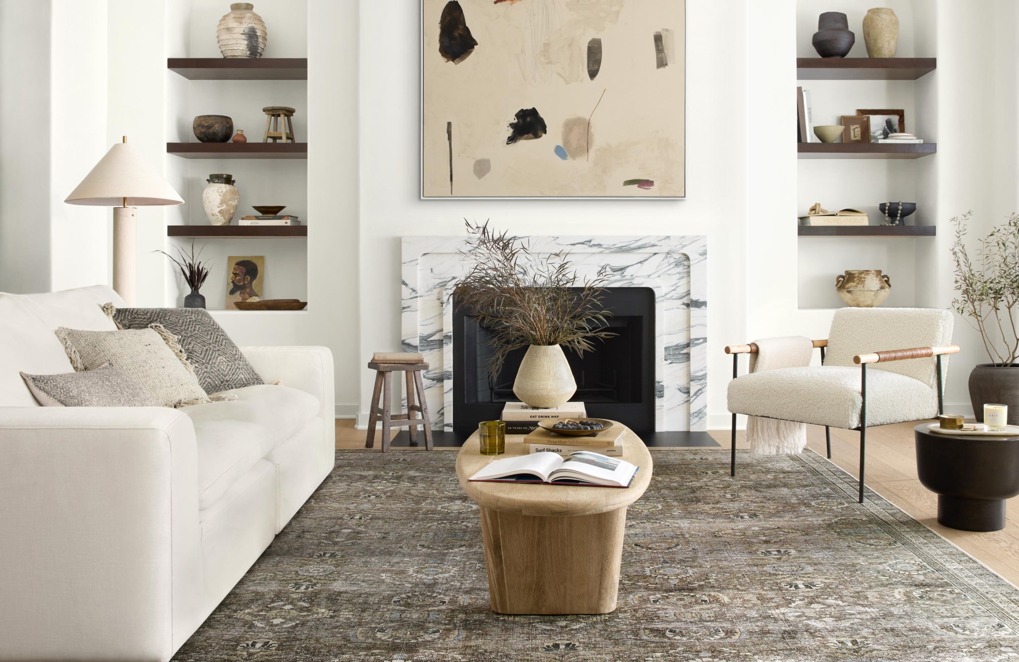 Cozy living room featuring a muted, ornate rug beneath a coffee table, paired with built-ins and a marble fireplace.