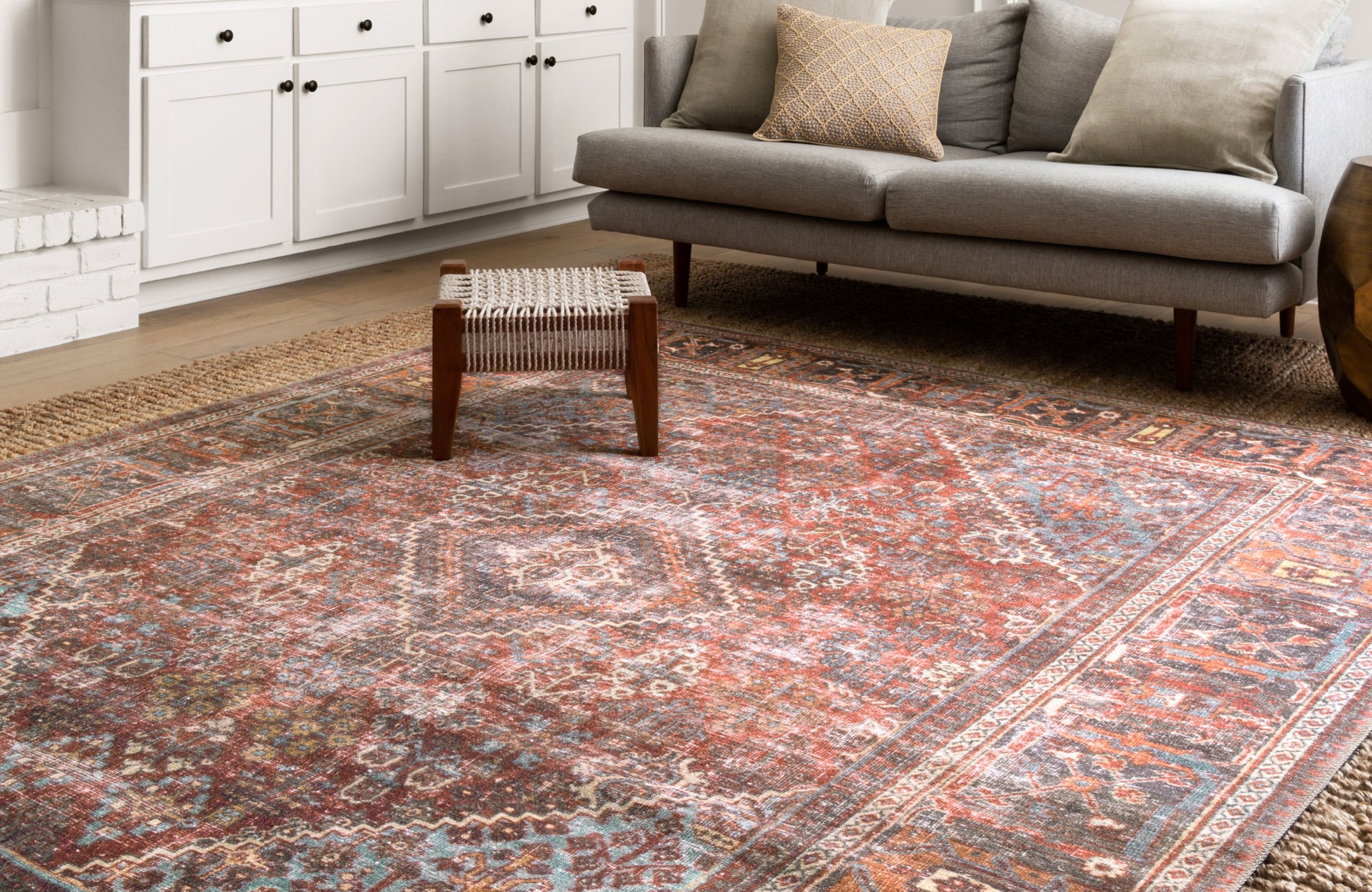 Layered rug look with a deep-toned vintage rug over natural jute, grounding a casual living space with warm textures.