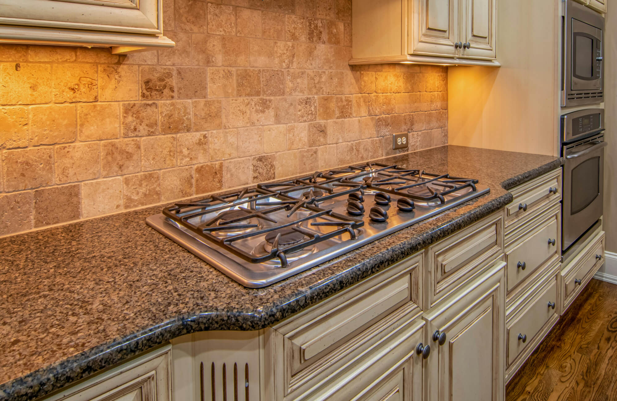 Luxurious kitchen with stone tile backsplash, granite countertops, and a modern stainless steel gas cooktop.