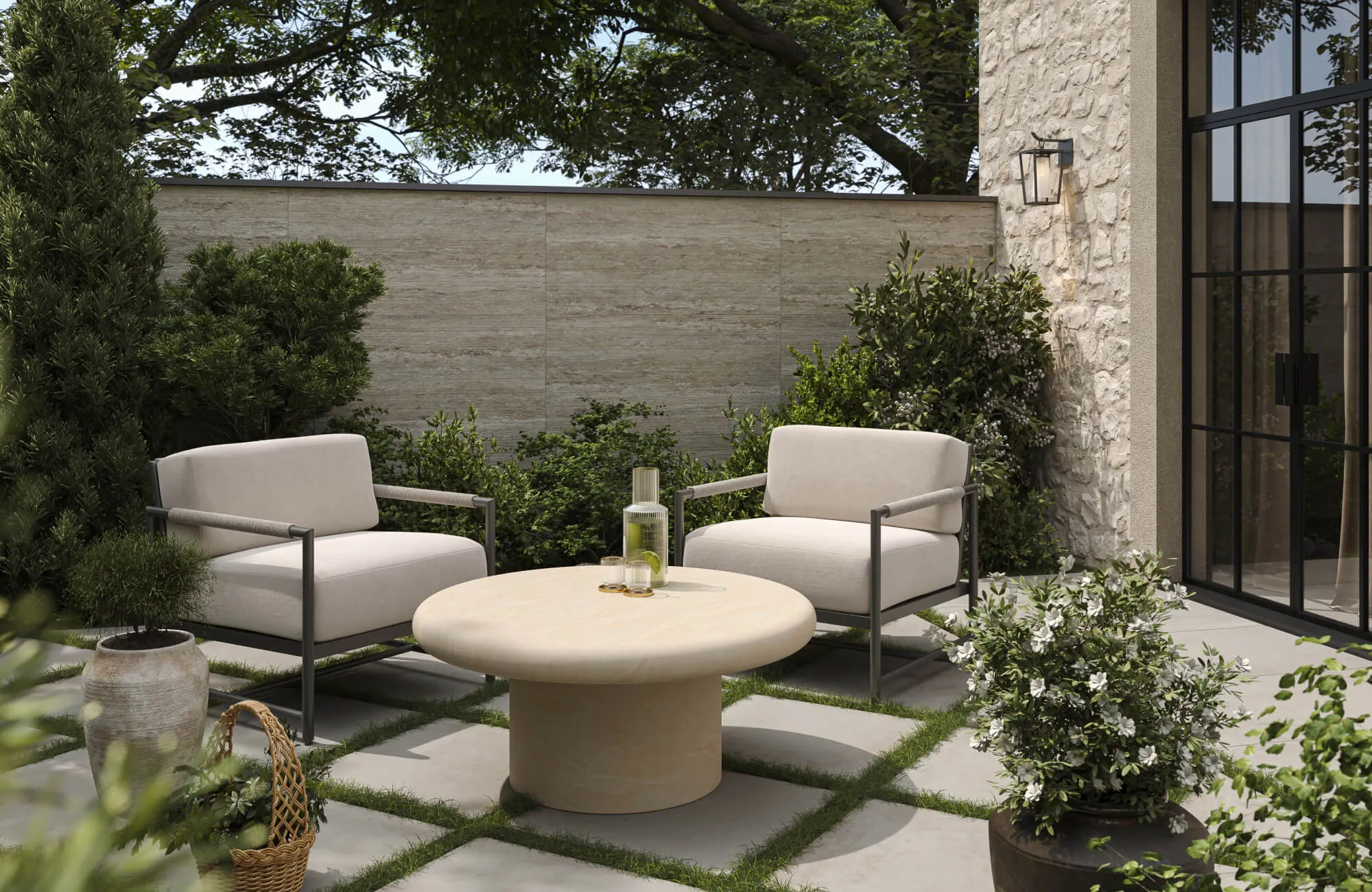 Modern outdoor patio with beige cushioned chairs, black metal frames, round beige stone table, and lush greenery.