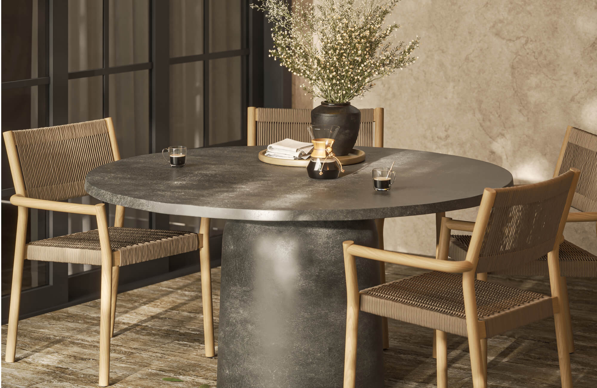 null Modern outdoor dining room with dark gray round table, light wood and brown woven chairs, and black decor accents.