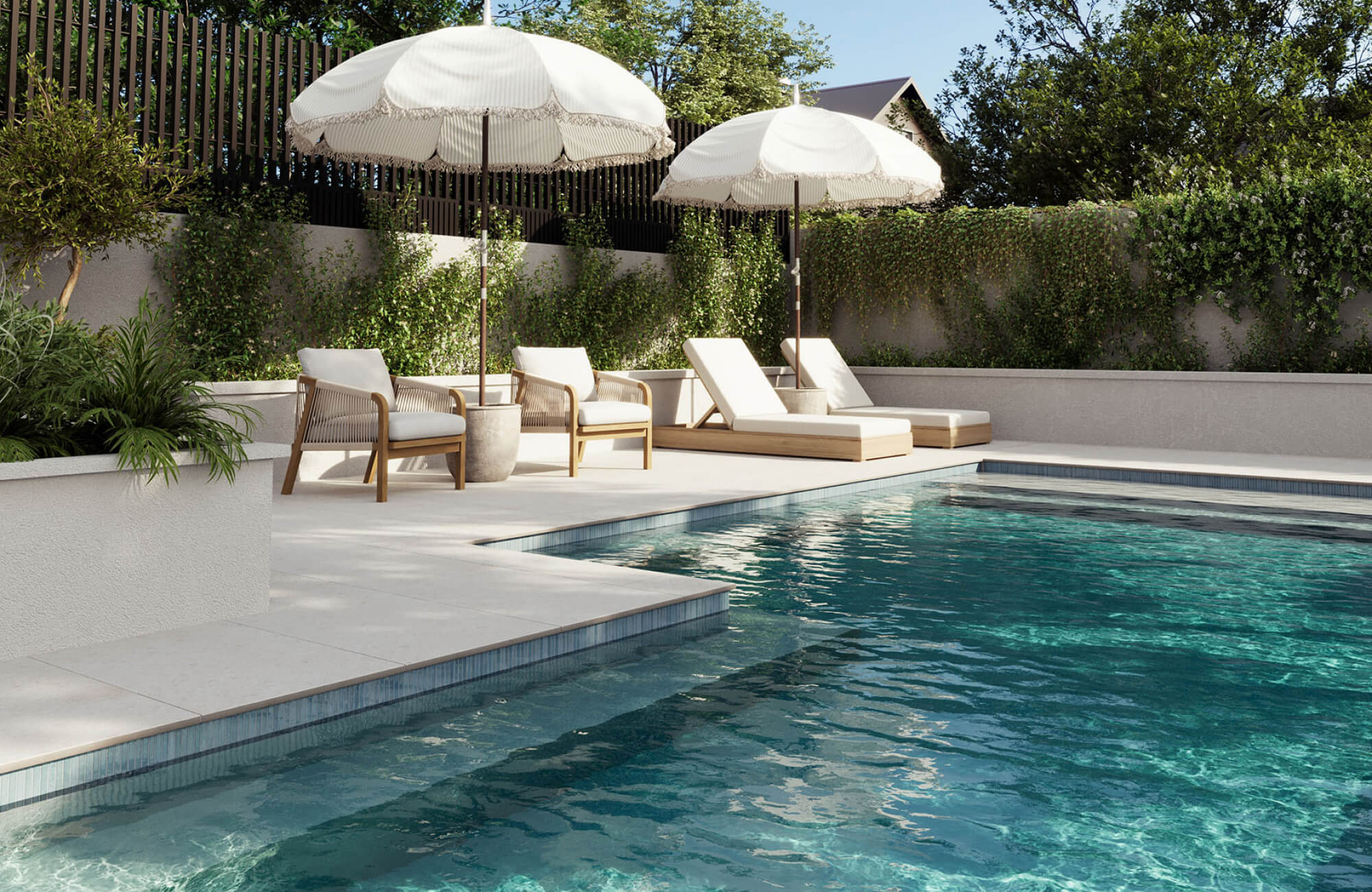 null White cushioned lounge chairs with warm wood frames and woven rope accent chairs surrounding a modern in-ground pool with light stone pavers, layered landscaping, and shaded seating areas