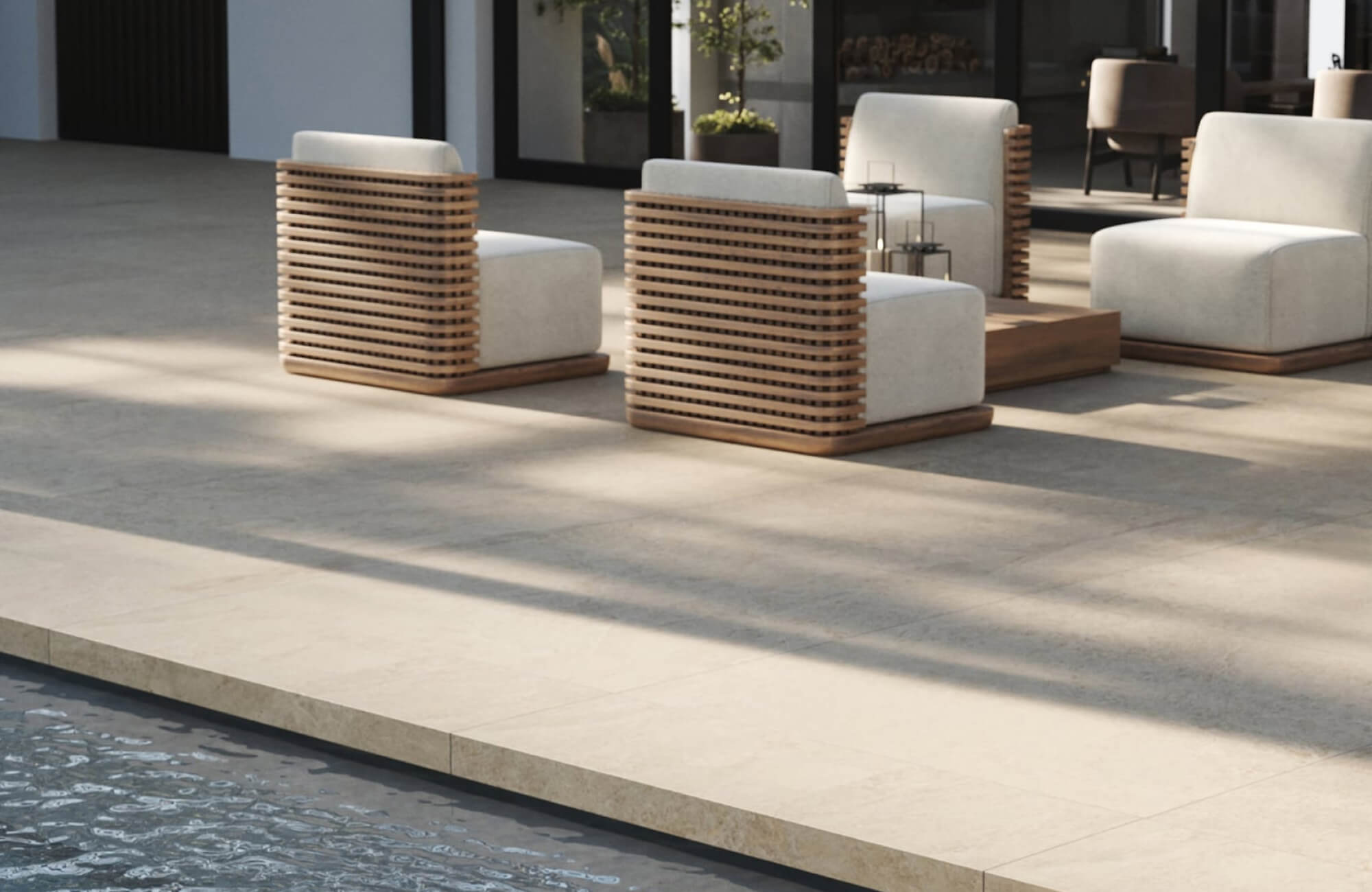 null Cream-colored chaise lounges with navy accent pillows positioned on a light stone pool deck surrounded by green lawn, trimmed hedges, and a dark tiled swimming pool in a contemporary backyard setting