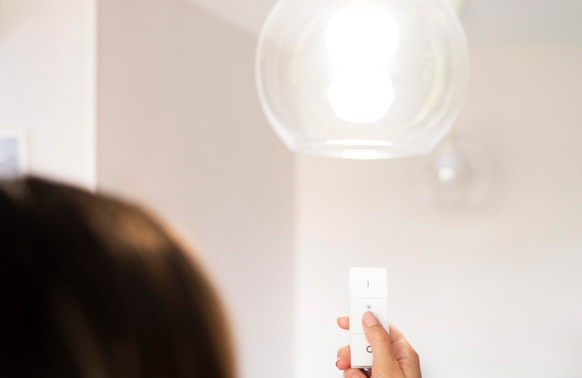 null Close-up of hand using a remote dimmer under a glowing glass pendant in a softly lit, minimalist interior.