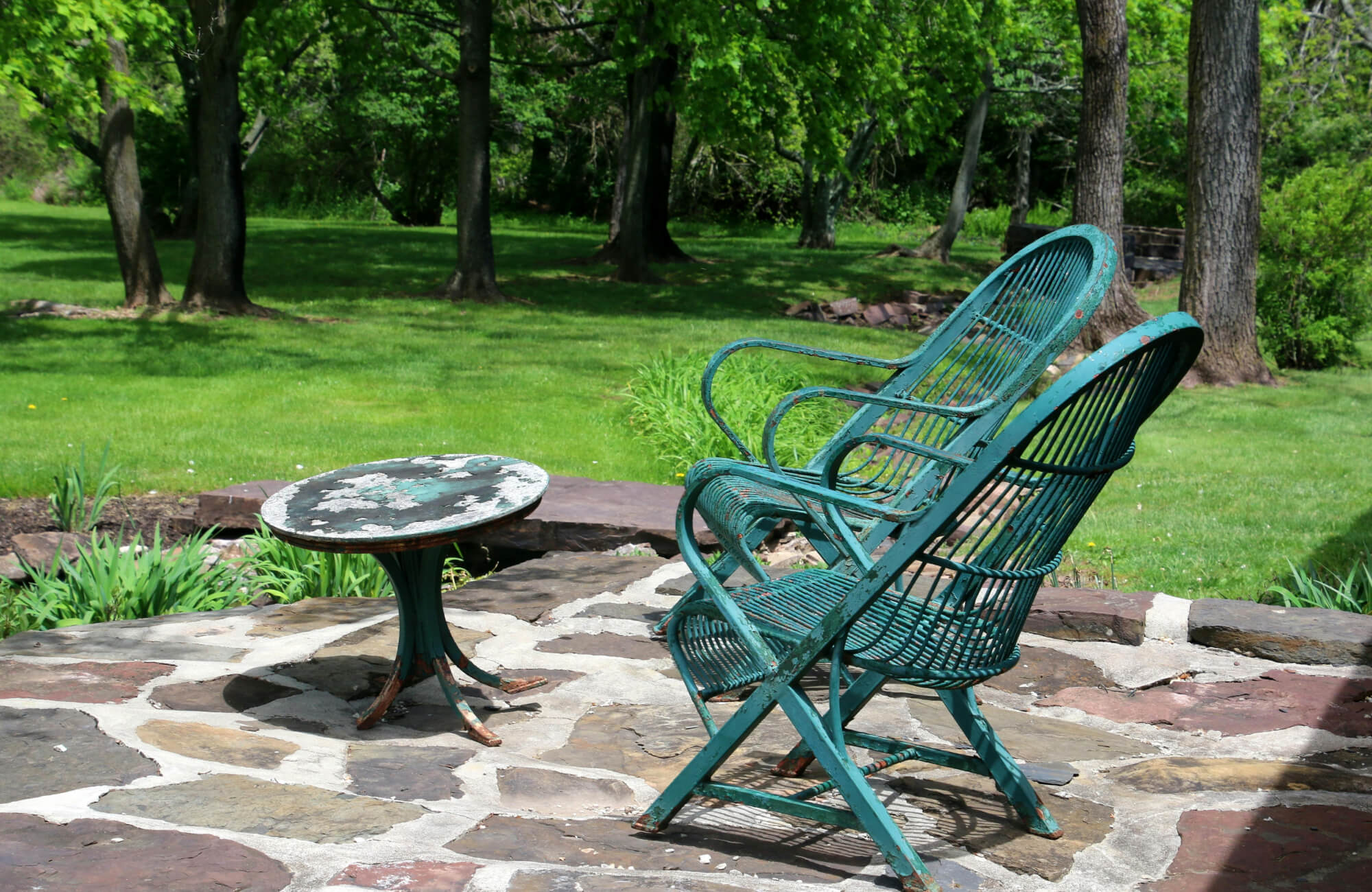 Weathered metal chair and table on a stone patio with peeling paint and rust, illustrating how outdoor materials break down from moisture and prolonged sun exposure