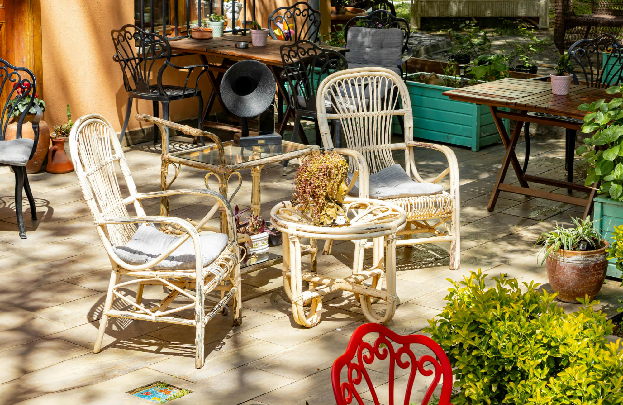 Mixed-material outdoor seating area with wicker, wood, and metal furniture on a garden patio, demonstrating varied material performance under constant outdoor conditions