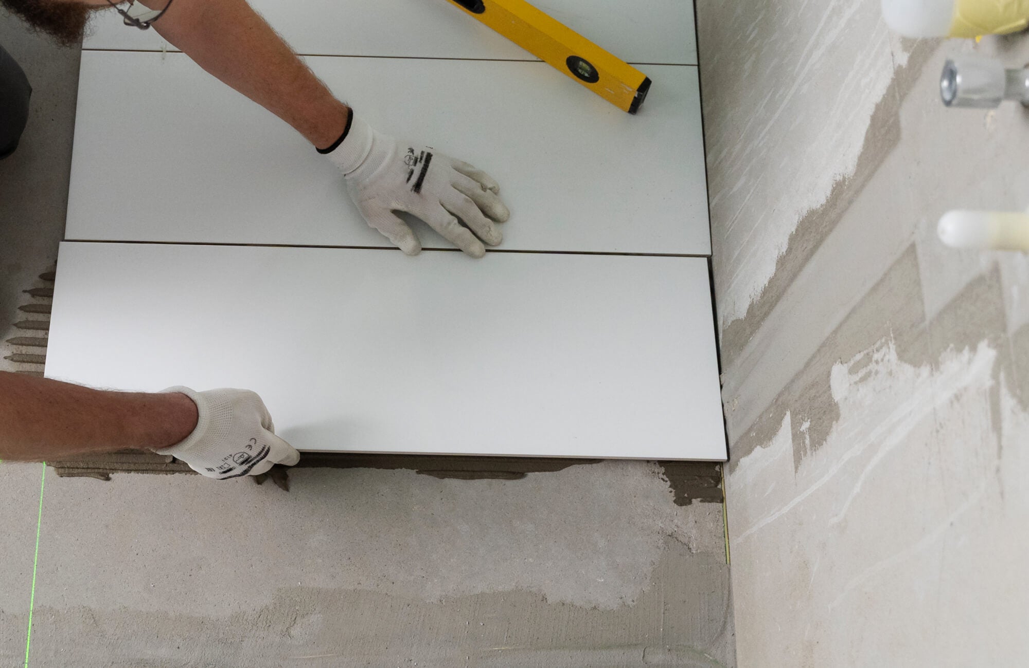 A professional installs white tiles with precision, using a leveling tool and adhesive to ensure a seamless and durable finish.