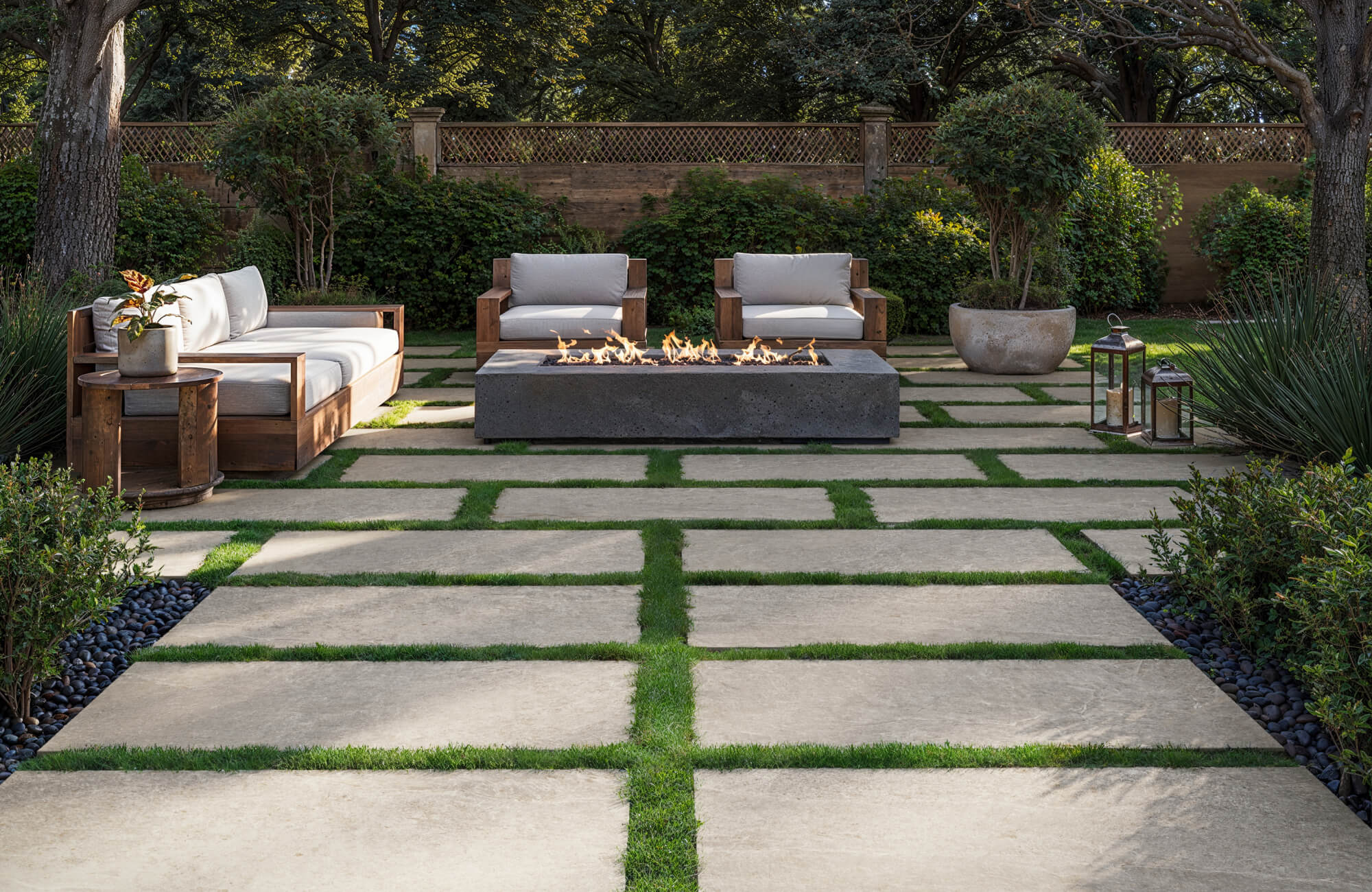A stylish outdoor lounge features large rectangular outdoor tile pavers set in a grid with lush grass joints, framing wood-accented seating and a modern linear fire pit surrounded by layered greenery.