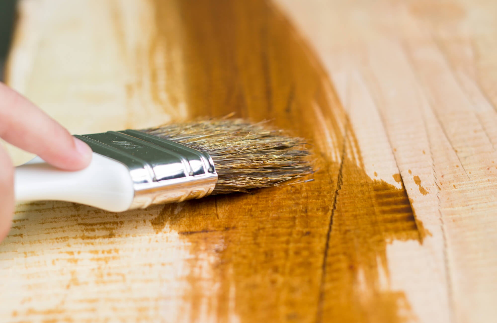 null A paintbrush applies a smooth layer of wood stain, highlighting the natural grain and enhancing the wood's rich tones.