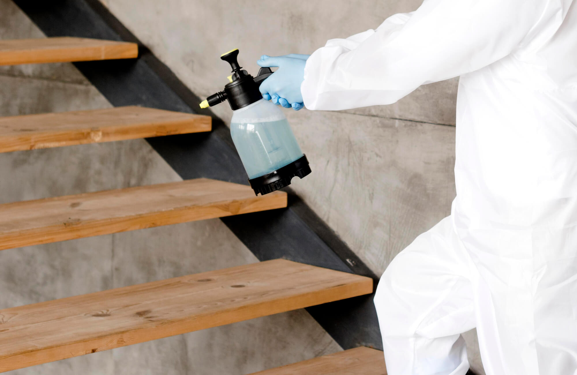 null A professional in protective gear applies a protective finish to wooden stairs using a spray bottle, ensuring durability and a polished look.
