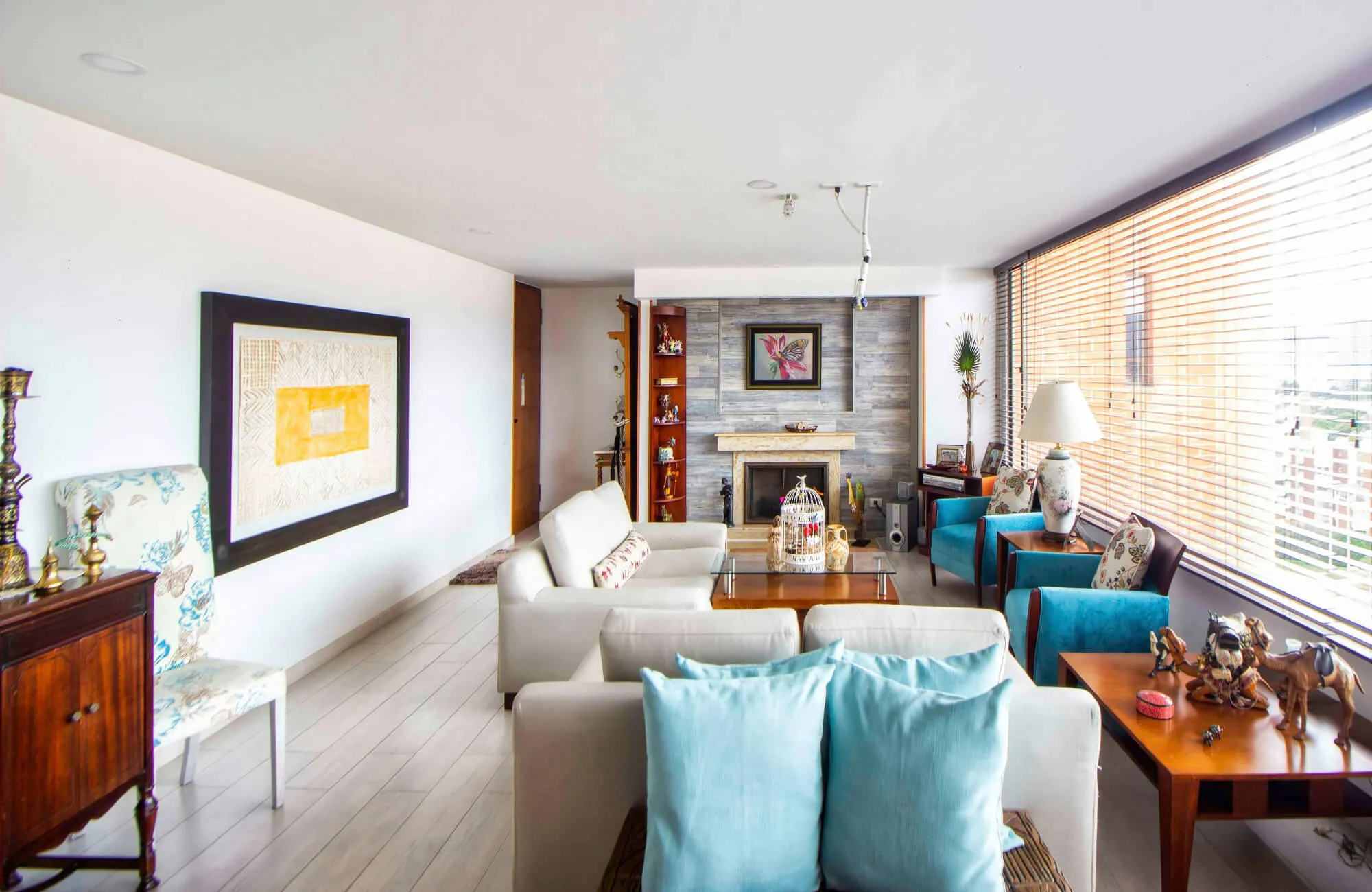 Bright living room with mixed wall art, neutral sofas, and teal chairs, creating a warm, layered space with natural light and decor accents.