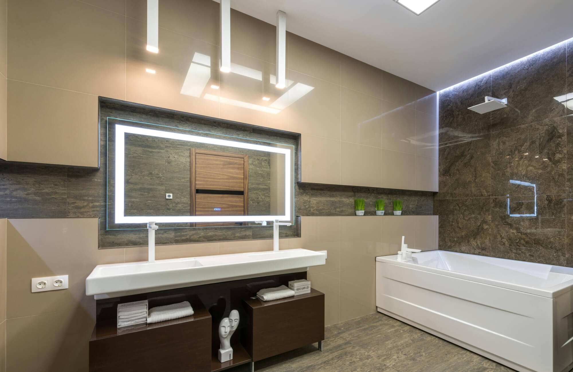 Contemporary bathroom featuring a large rectangular LED backlit mirror, floating double sink vanity, glossy tile walls, and integrated ambient lighting