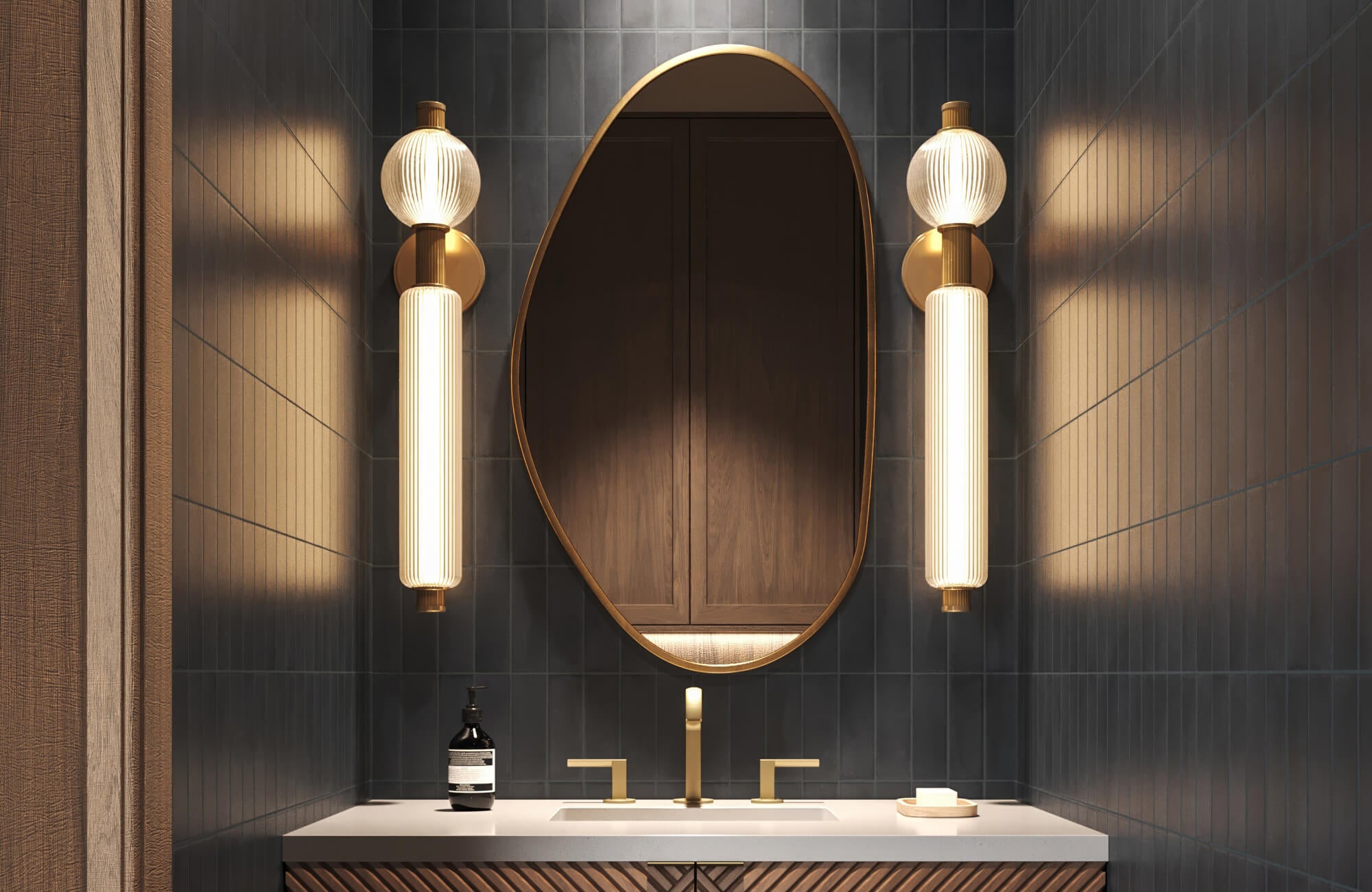 Moody bathroom with trendy asymmetrical oval mirror, dramatic brass and ribbed glass sconces, dark vertical tile walls, and fluted wood vanity