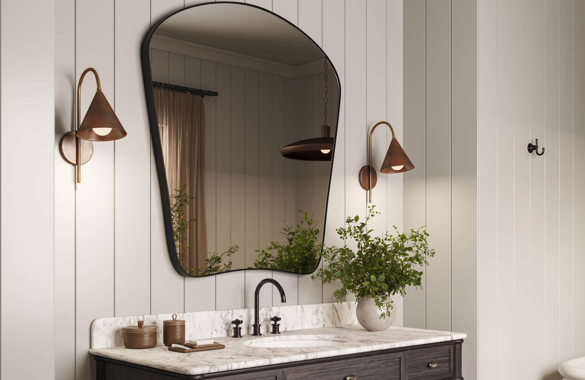 Modern bathroom mirror with an organic black frame hangs above a marble vanity, flanked by sleek bronze sconces and accented with greenery for a warm, stylish touch.
