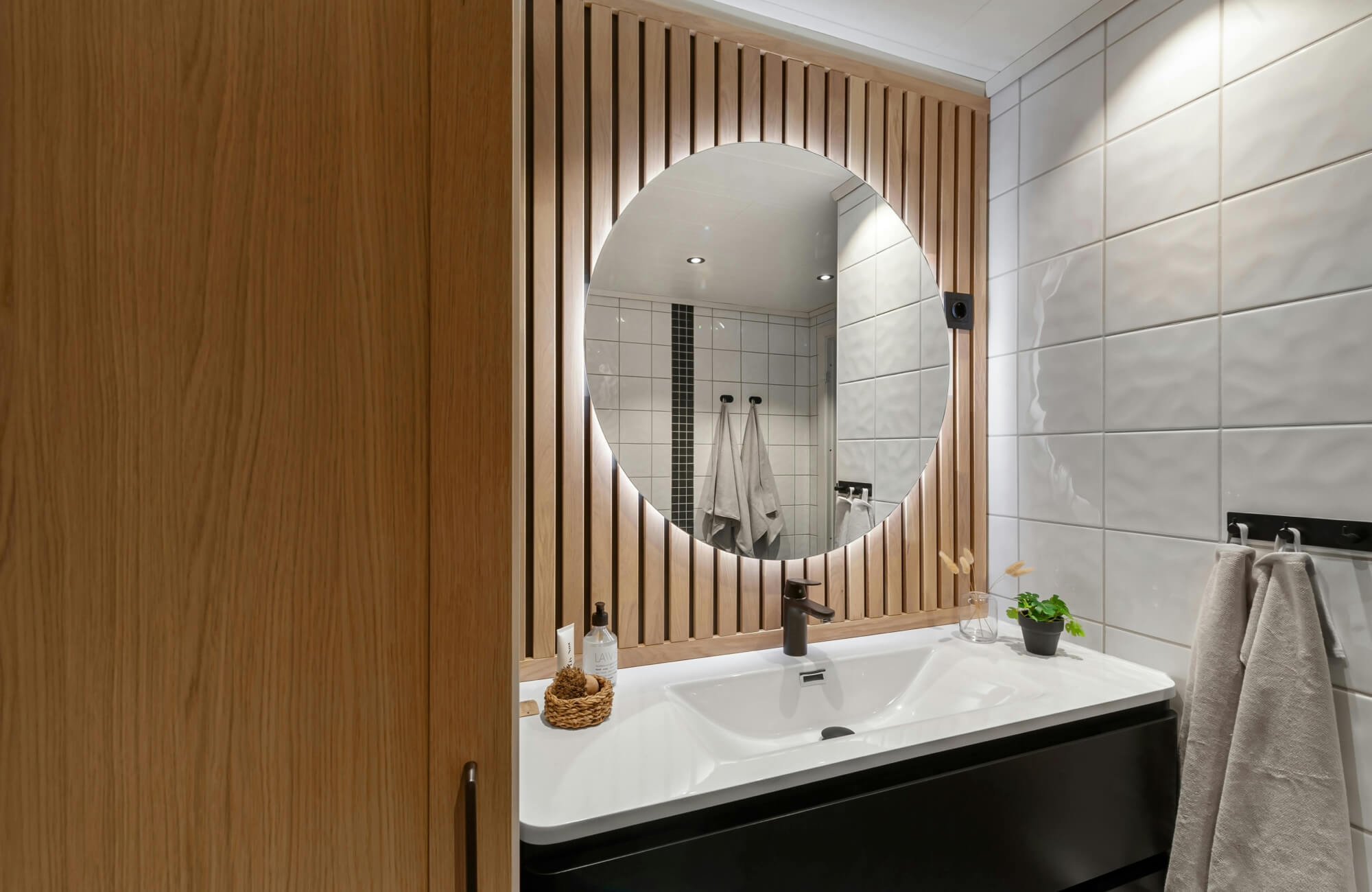 null Warm backlit round mirror highlighting wood slat wall above a modern vanity in a cozy bathroom.