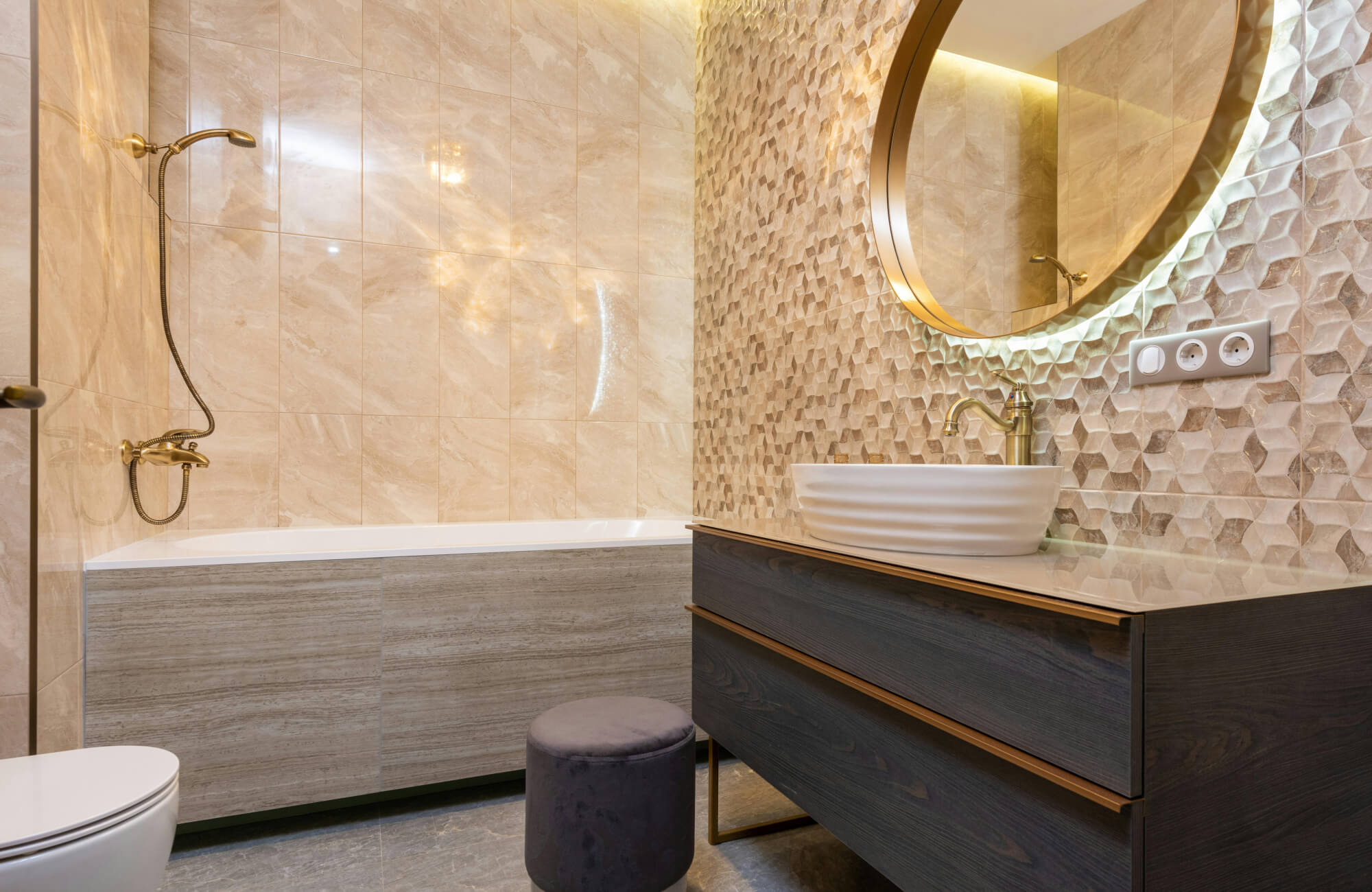 null Warm backlit mirror casting a halo over textured tile wall beside a bathtub in a modern bathroom.