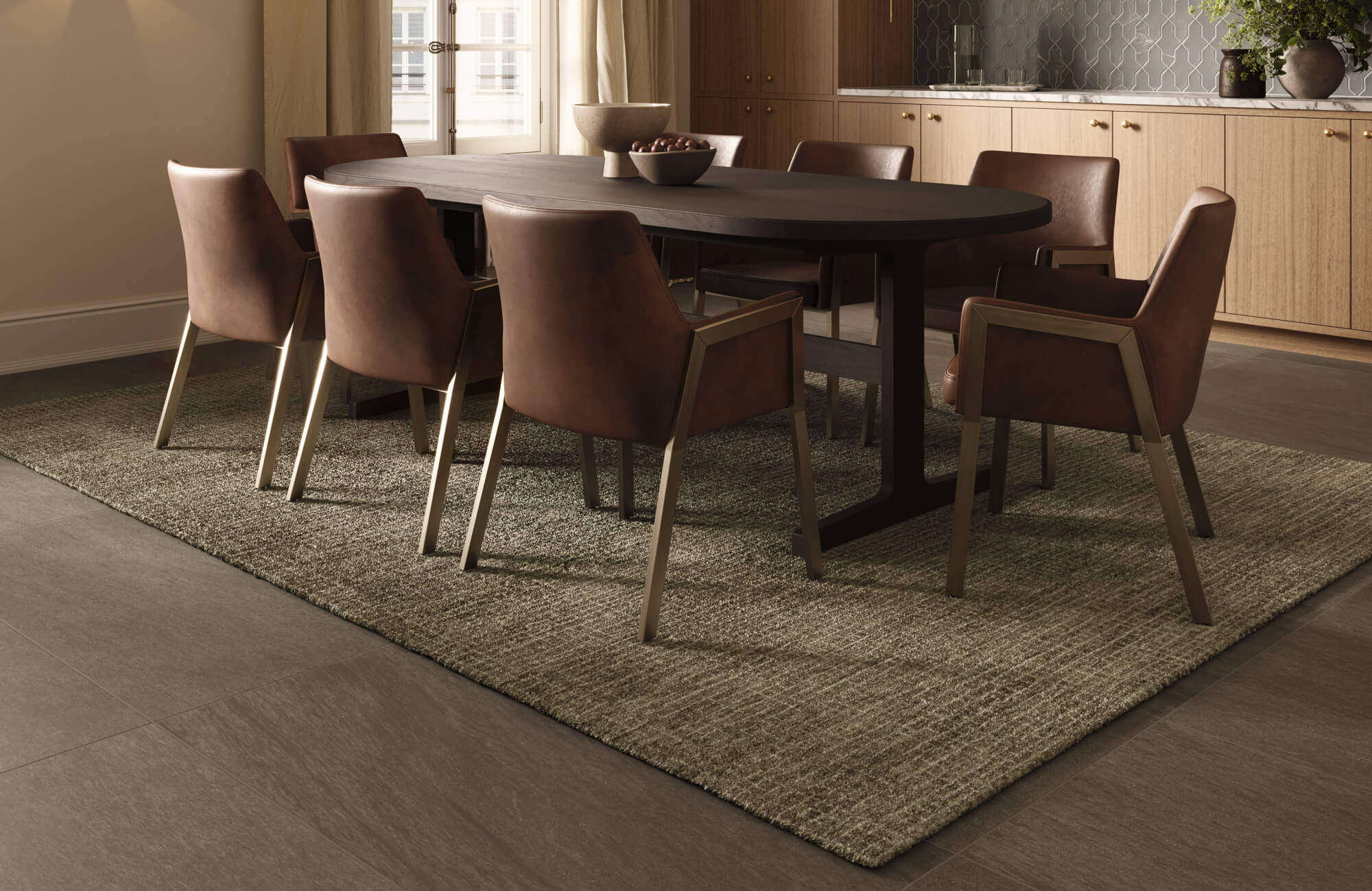 Sophisticated dining room with dark tile flooring, an olive textured area rug, a black oval table, and brown leather chairs.